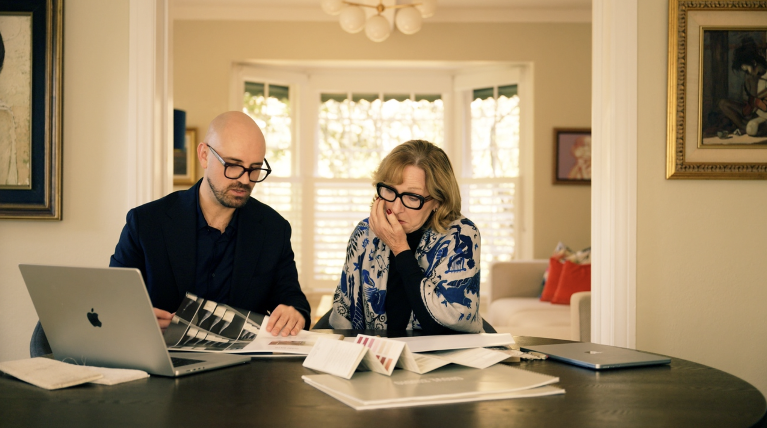 Two adults reviewing documents at a dining table with laptops and paperwork