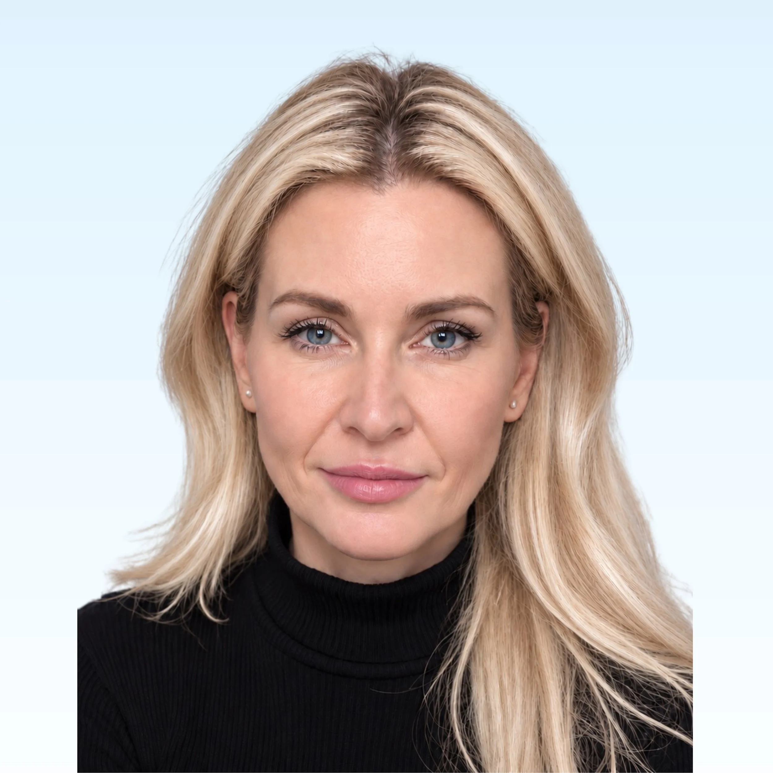 Portrait of a woman with long blonde hair wearing a black blazer and a gray sweater against a light blue background.