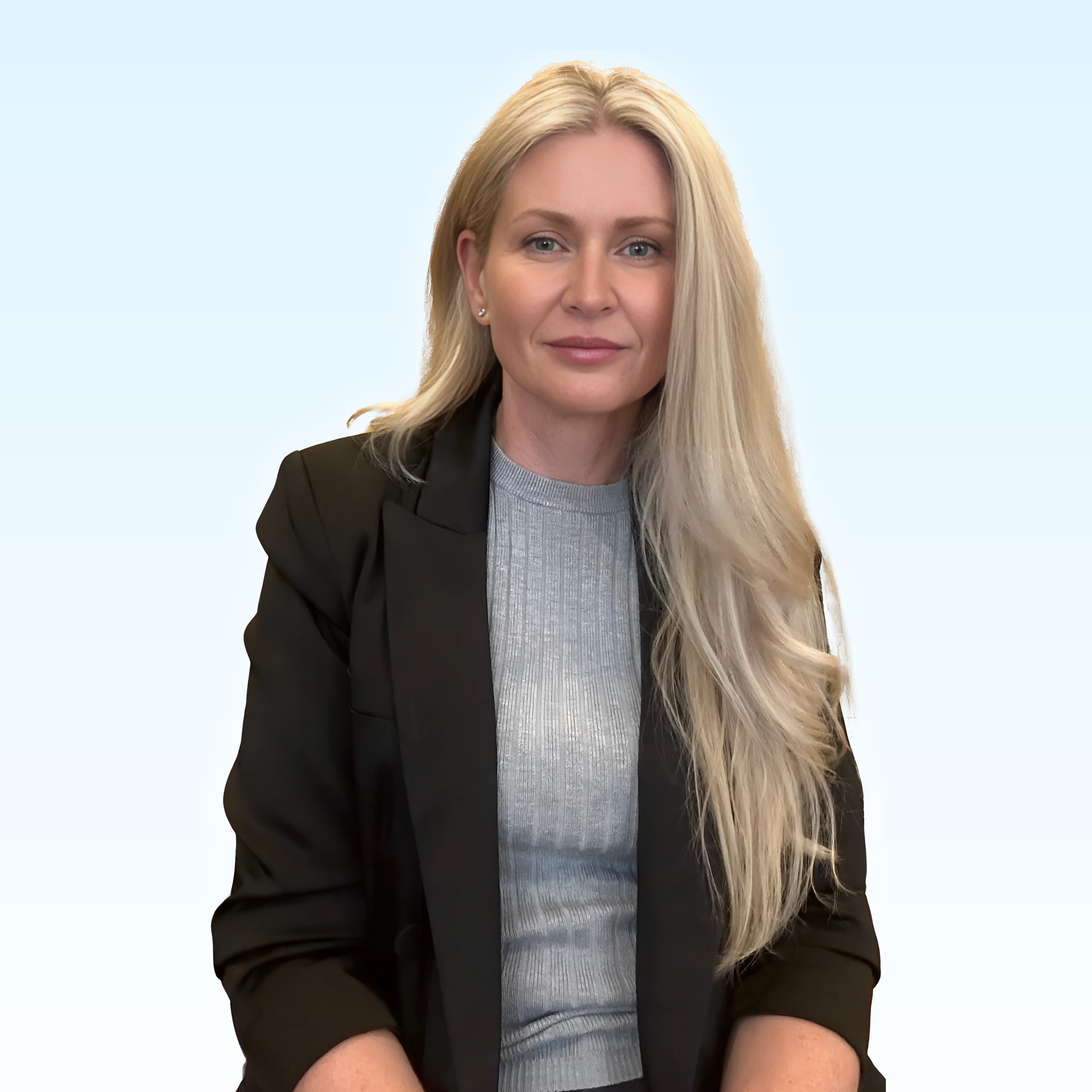 Portrait of a woman with long blonde hair wearing a black blazer and a gray sweater against a light blue background.