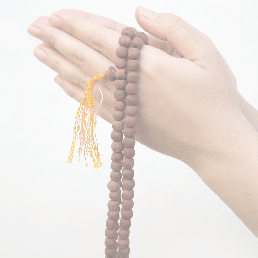 Main tenant des mains jointes tenant un chapelet en bois avec une tassette jaune, se préparant à la méditation.