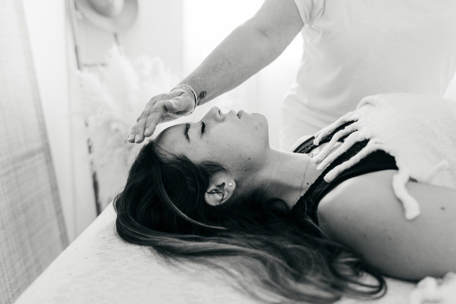 Une femme allongée sur une table, recevant un soin reiki ou une thérapie, avec une main d'un praticien reiki posée sur son front, dans un environnement de bien-être.