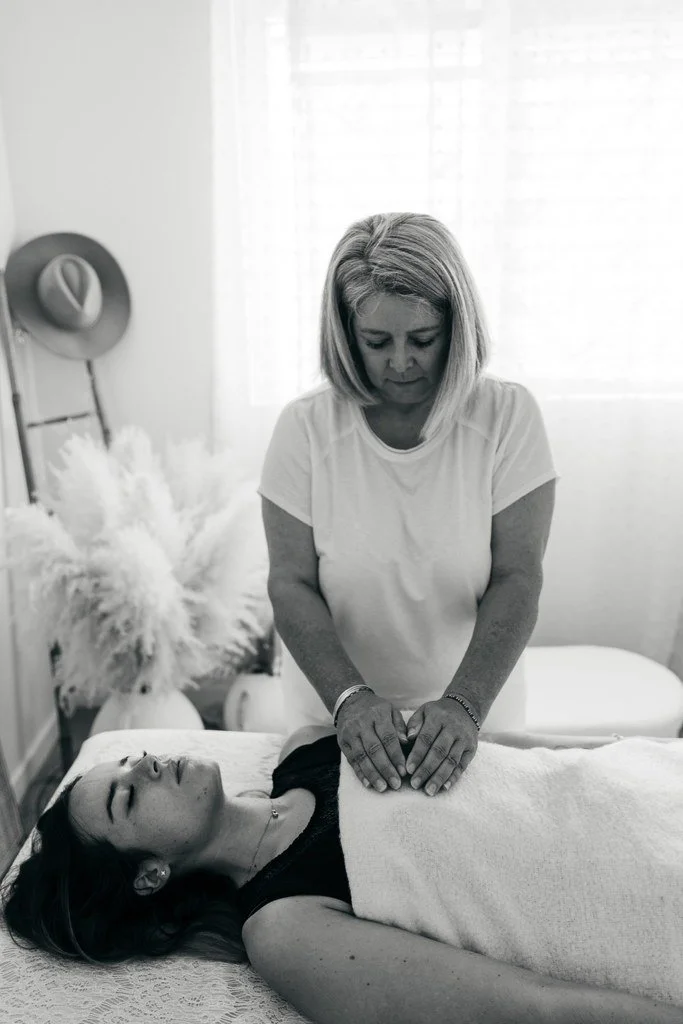 Une femme donne un soin énergétique reiki  à une autre femme allongée sur une table de soin dans une pièce lumineuse.