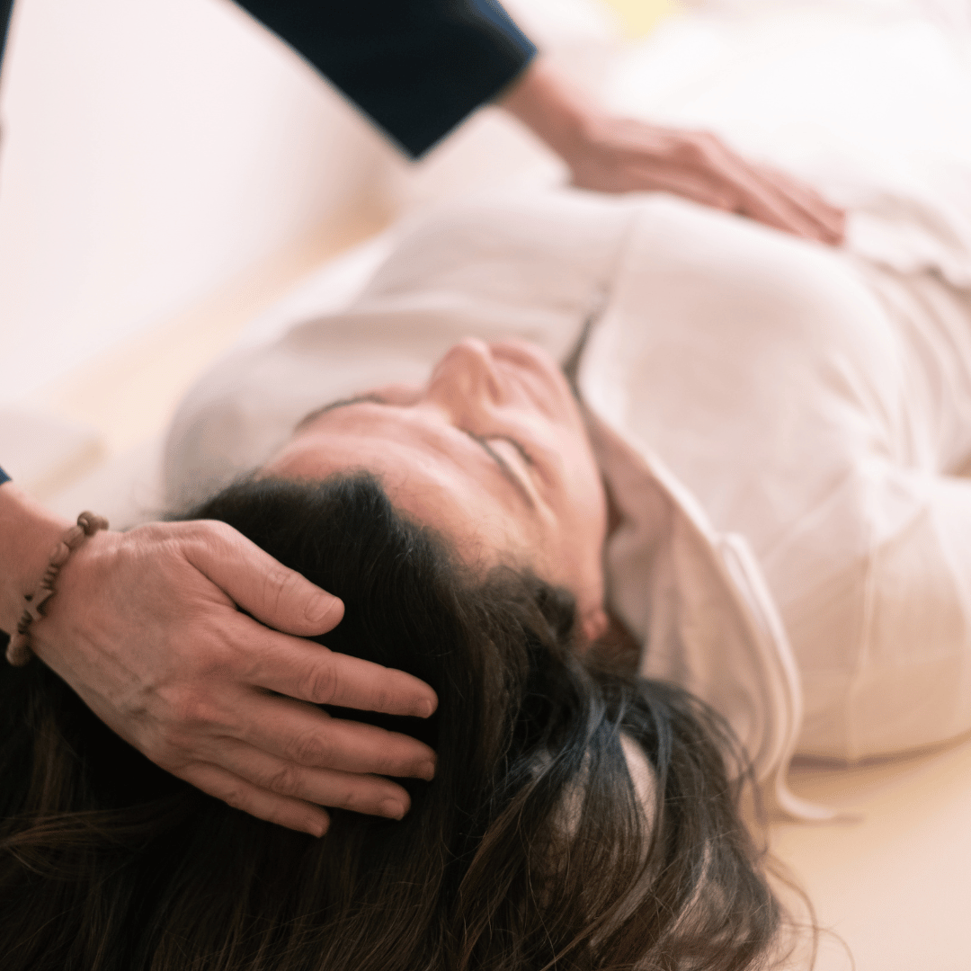 Une femme allongée, recevant une technique de soin énergétique reiki aux chakra couronne  par une personne non visible, dans un environnement intérieur apaisant.