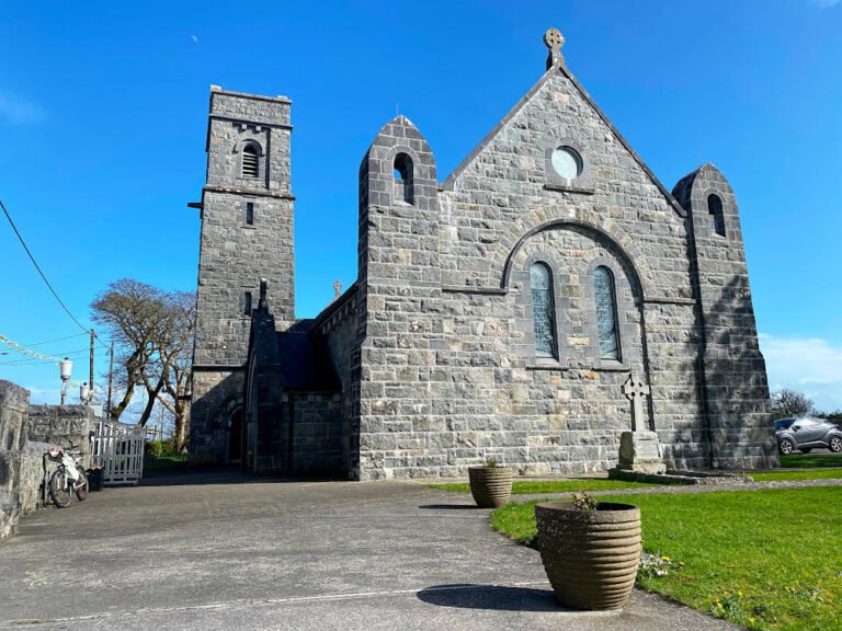 Stone church with tower, arched windows, and grassy area in front.