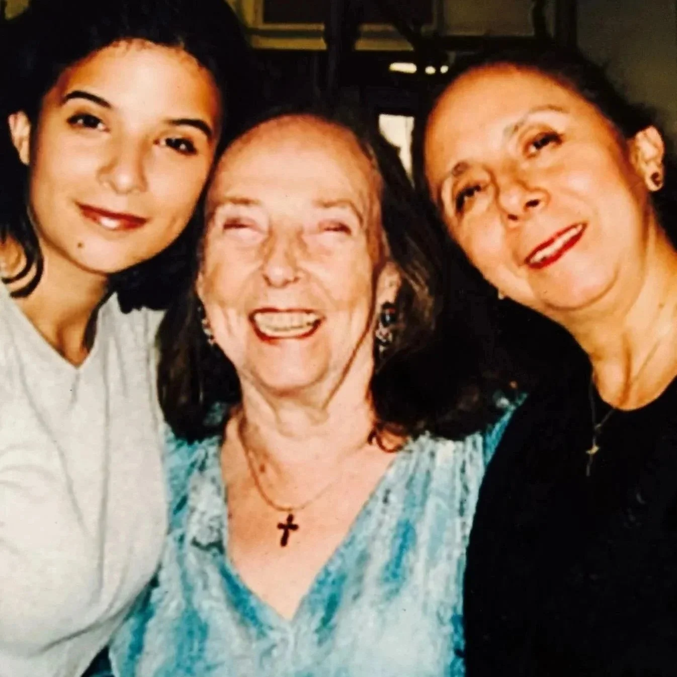 Alt Text: Three generations of women, including a young woman, a middle-aged woman, and a laughing older woman in the center, smile closely together.