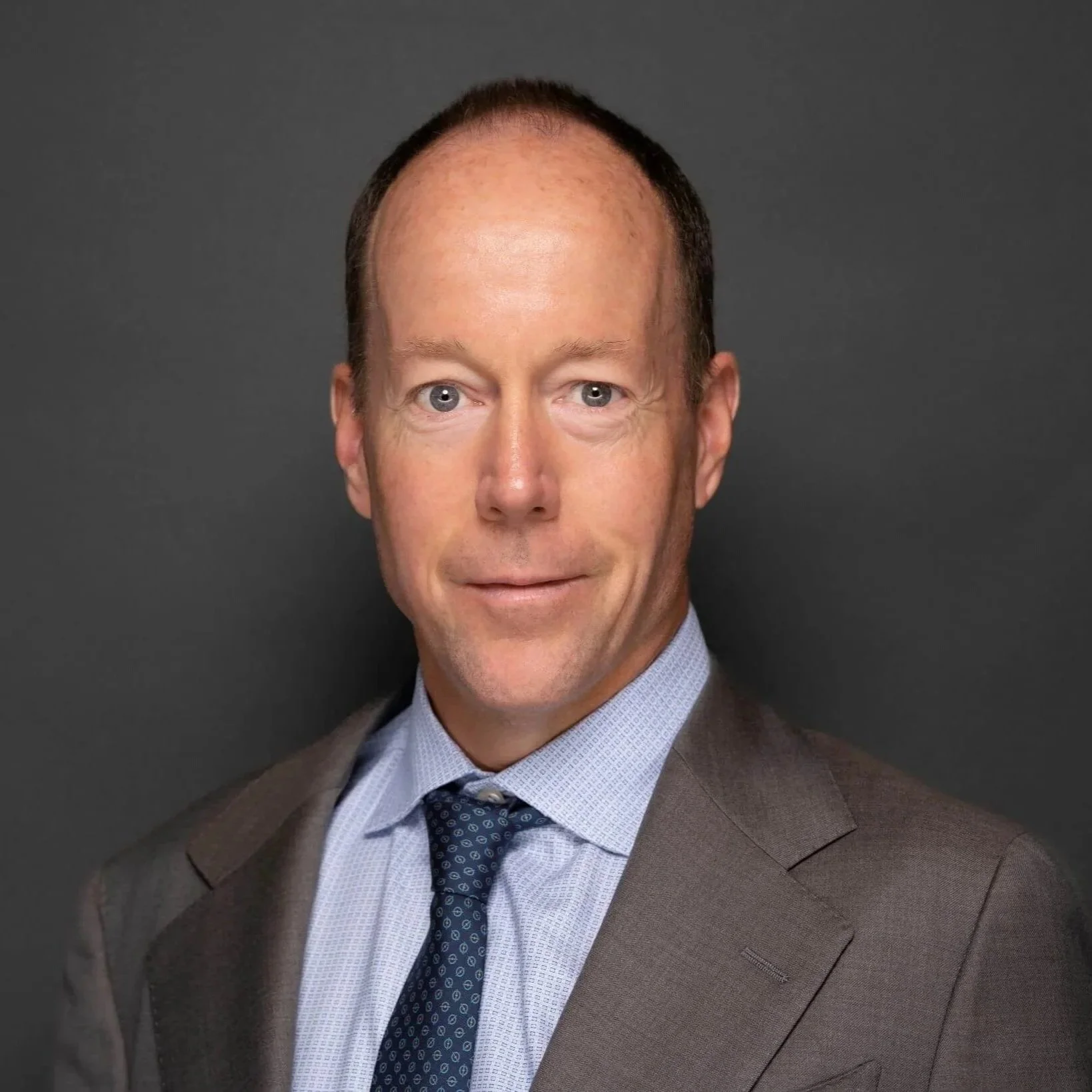 Professional headshot of a man in a suit against a dark background.