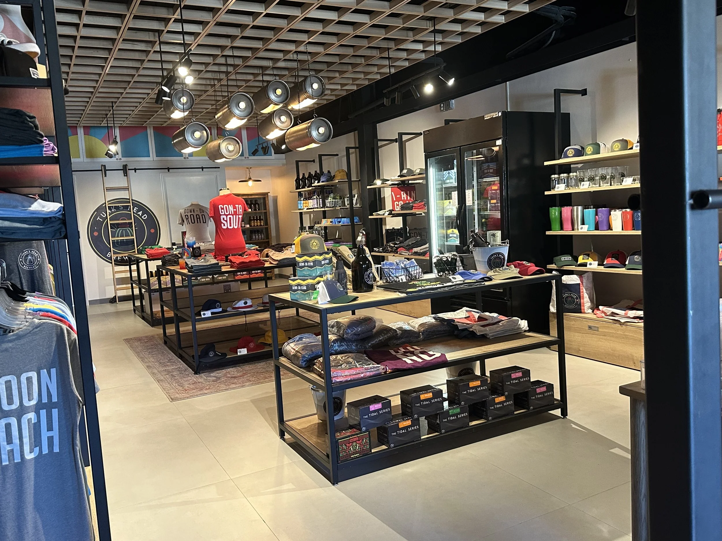 Display of Island Draught apparel and accessories related to Turk's Head, including polo shirts, hats, and T-shirts with beer and island themes, along with colorful wall art featuring beer and island references.