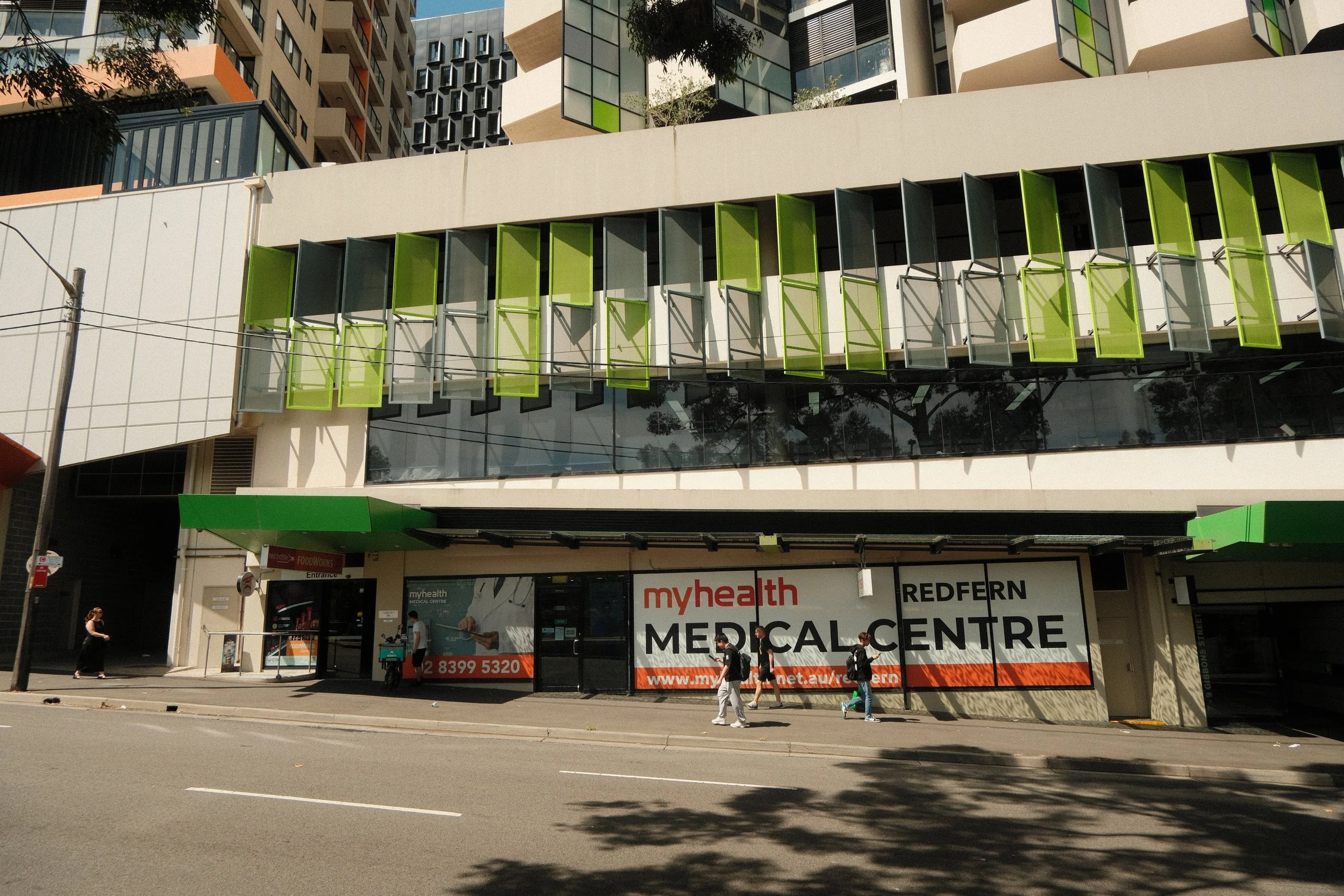 Street view of a modern medical center with green window accents and a large sign that reads 'myhealth REDFERN MEDICAL CENTRE'.