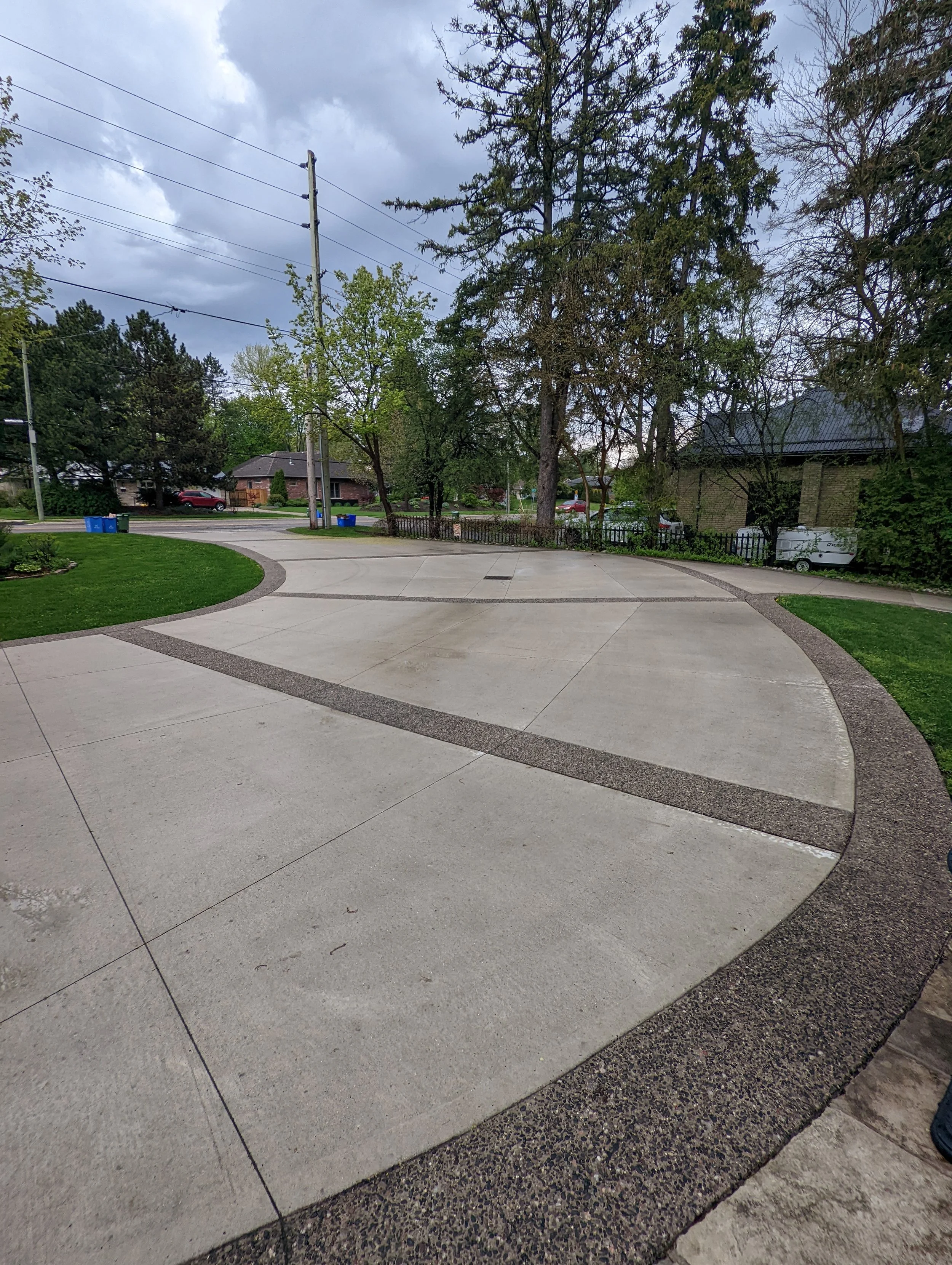 Concrete driveway with patterned edges in a residential area, surrounded by trees and greenery.