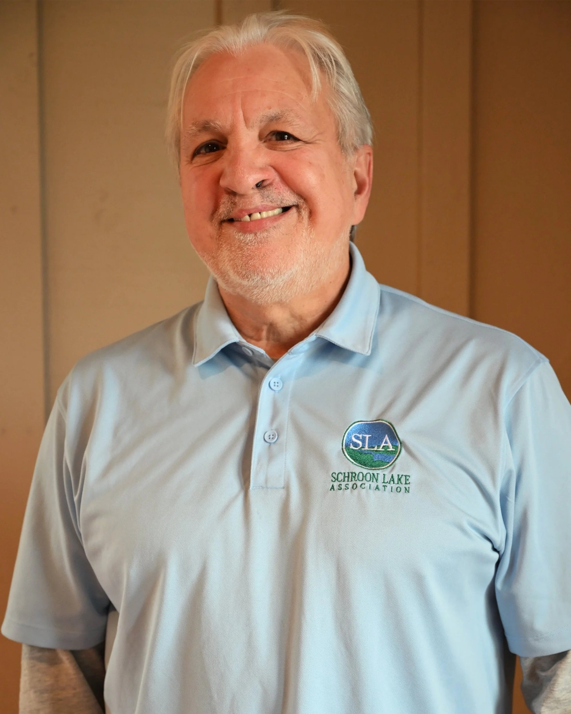 Smiling older man wearing a light blue polo shirt with Schroon Lake Association logo.