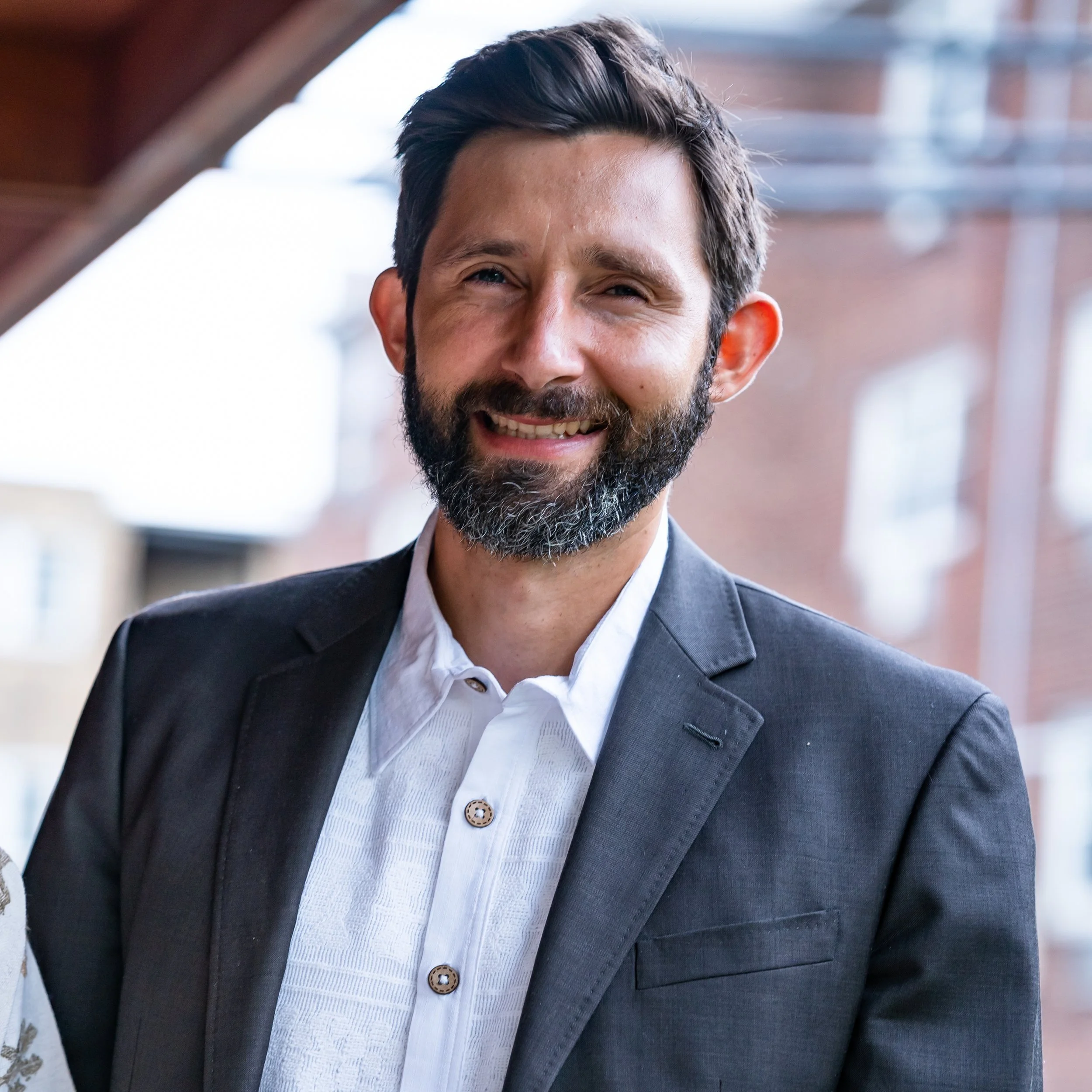 Man with beard smiling in suit outdoors
