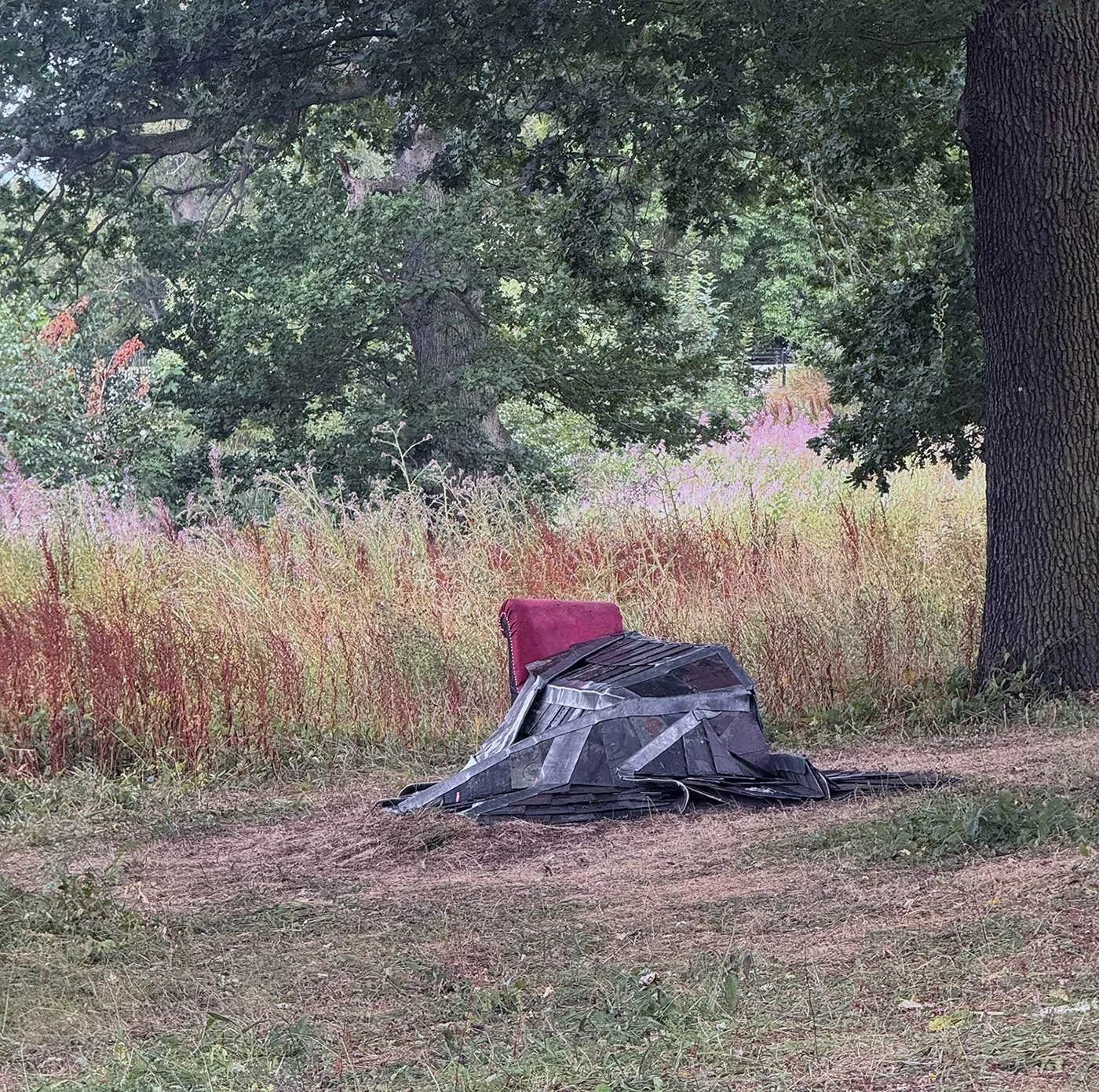 Photograph of a grey stiched slate quilt draped on a red chaise longue  - Andi Walkers new outdoor sculpture 'Wrapped in Cold Hard Comfort' at Yorkshire Sculpture Park