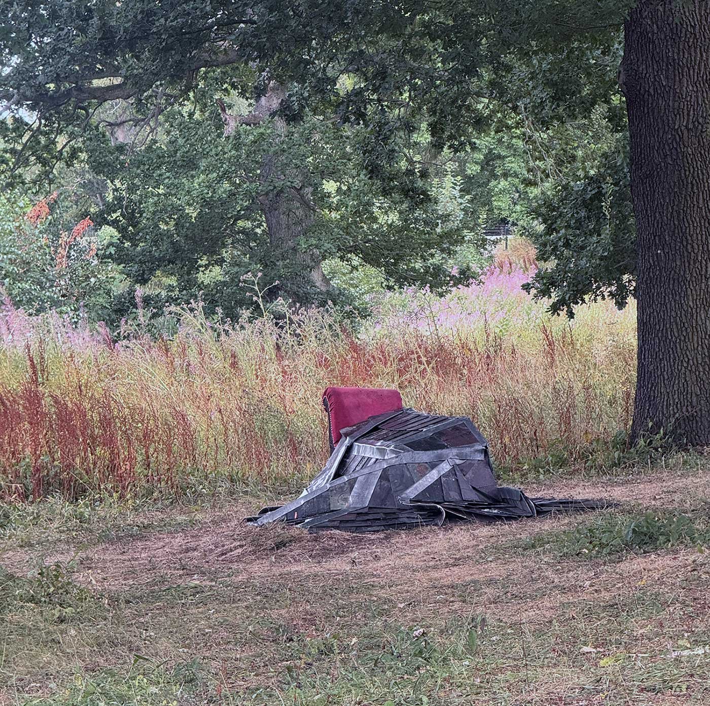 Photograph of a grey stiched slate quilt draped on a red chaise longue  - Andi Walkers new outdoor sculpture 'Wrapped in Cold Hard Comfort' at Yorkshire Sculpture Park