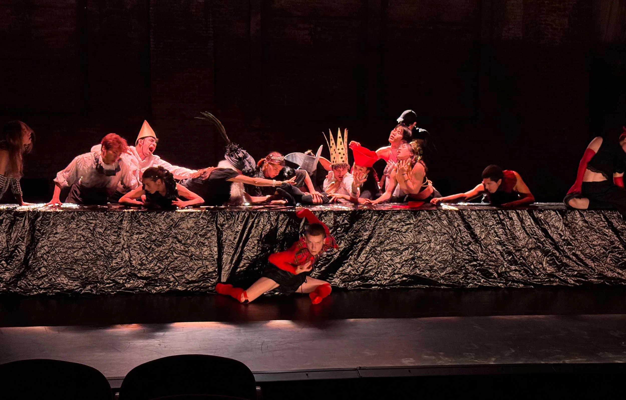 Spotlit in the darkness dancers with crowns writhe over a long table