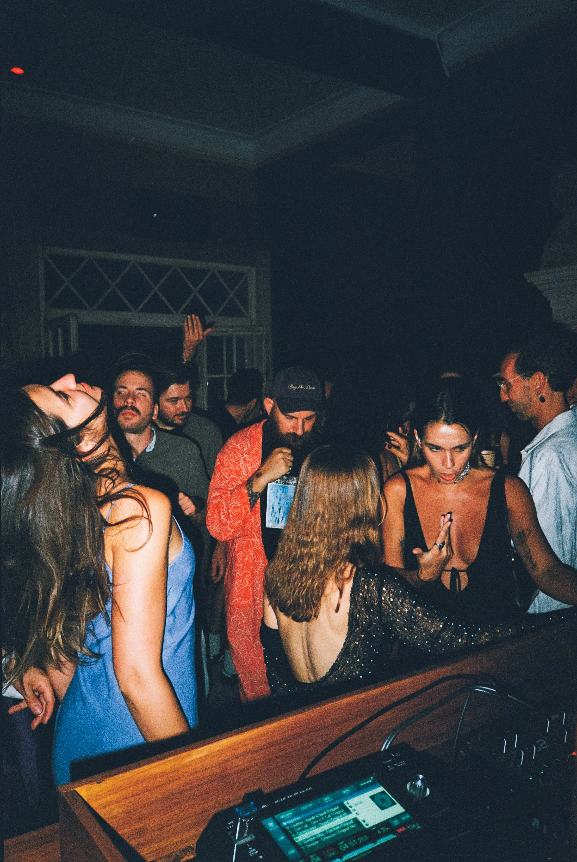 People dancing and socializing at a party with a DJ booth in the foreground.