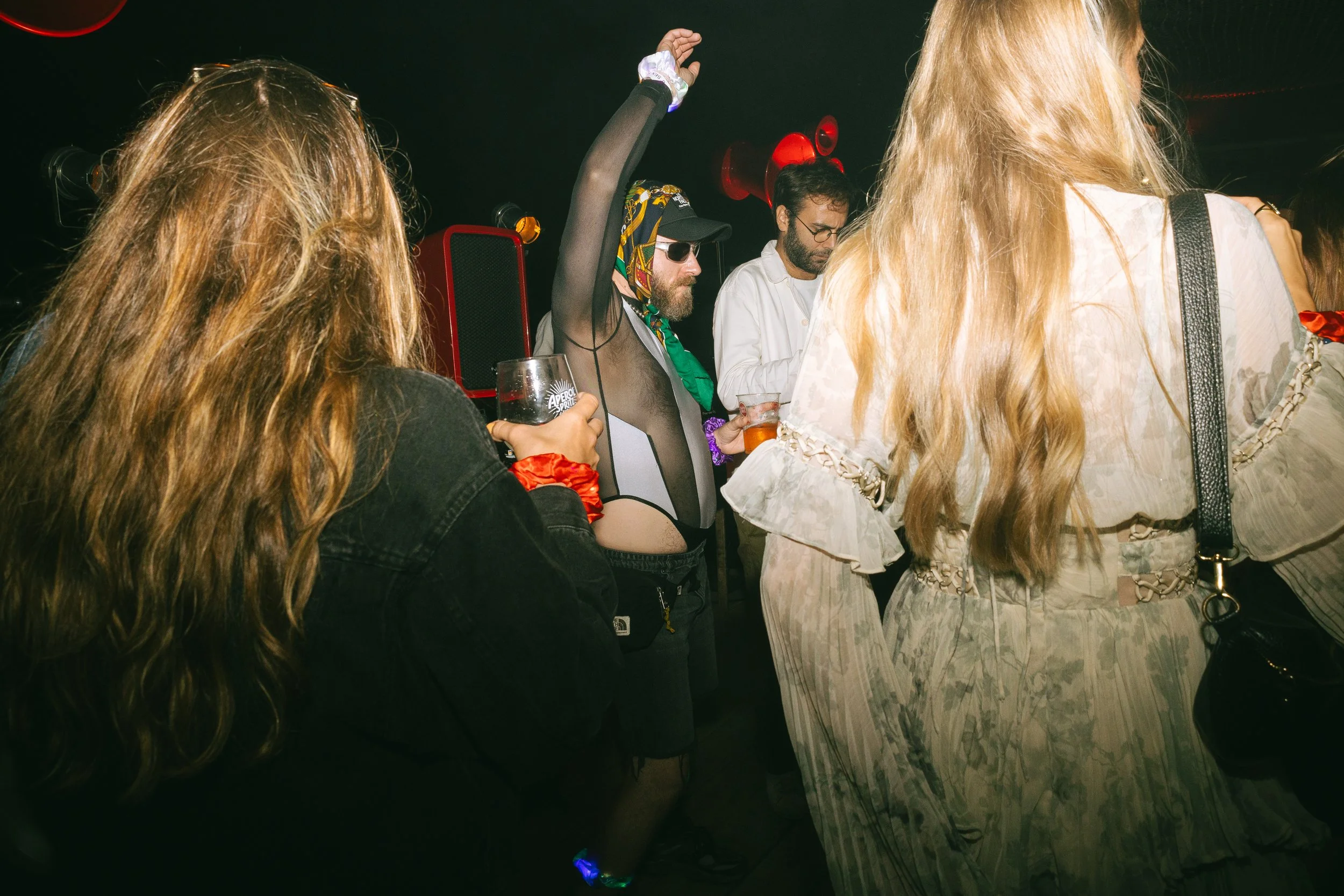 People dancing and socializing at a party or nightclub with drinks in hand, colorful lighting, and a lively atmosphere.