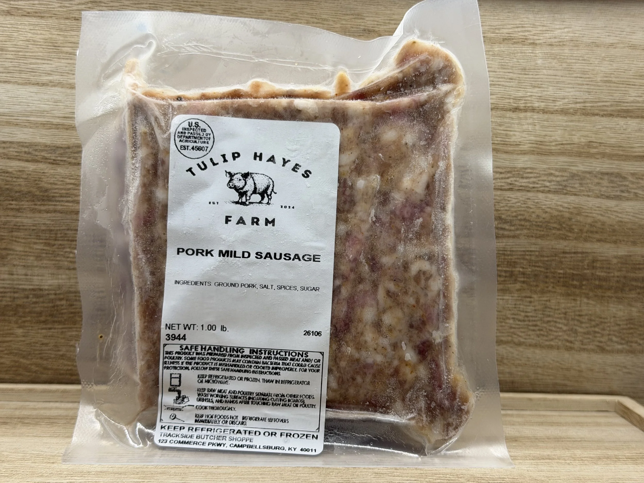 Vacuum-sealed package of raw pork mild sausage from Tulip Hayes Farm, placed on a wooden surface.