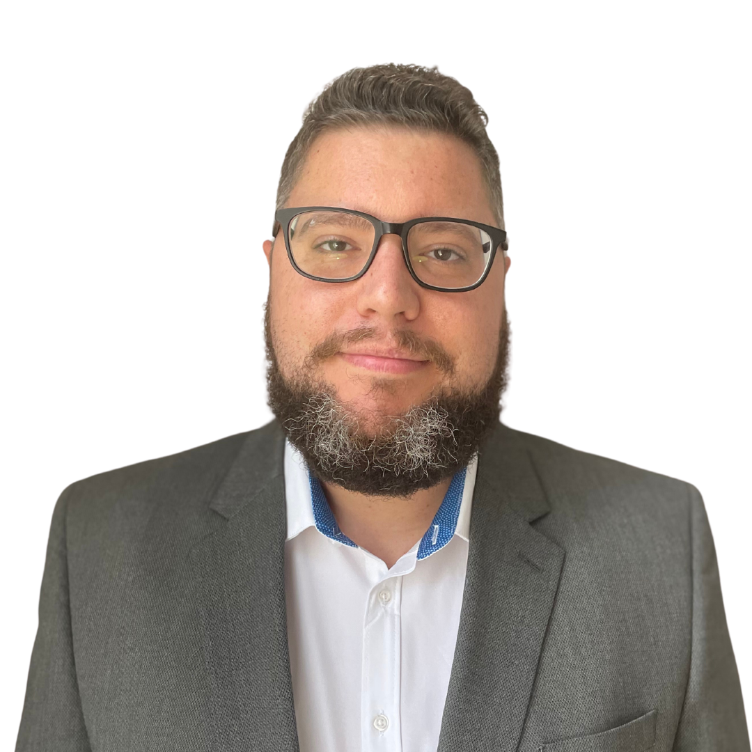Headshot of a man with glasses, a beard, wearing a suit and white shirt, against a blue background.