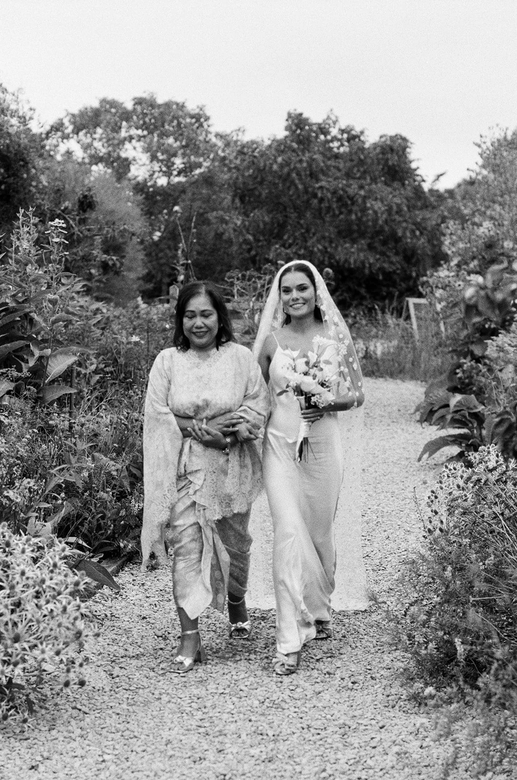 A bride walking with her mum down the aisle for their outdoor wedding ceremony at Worton Kitchen Garden