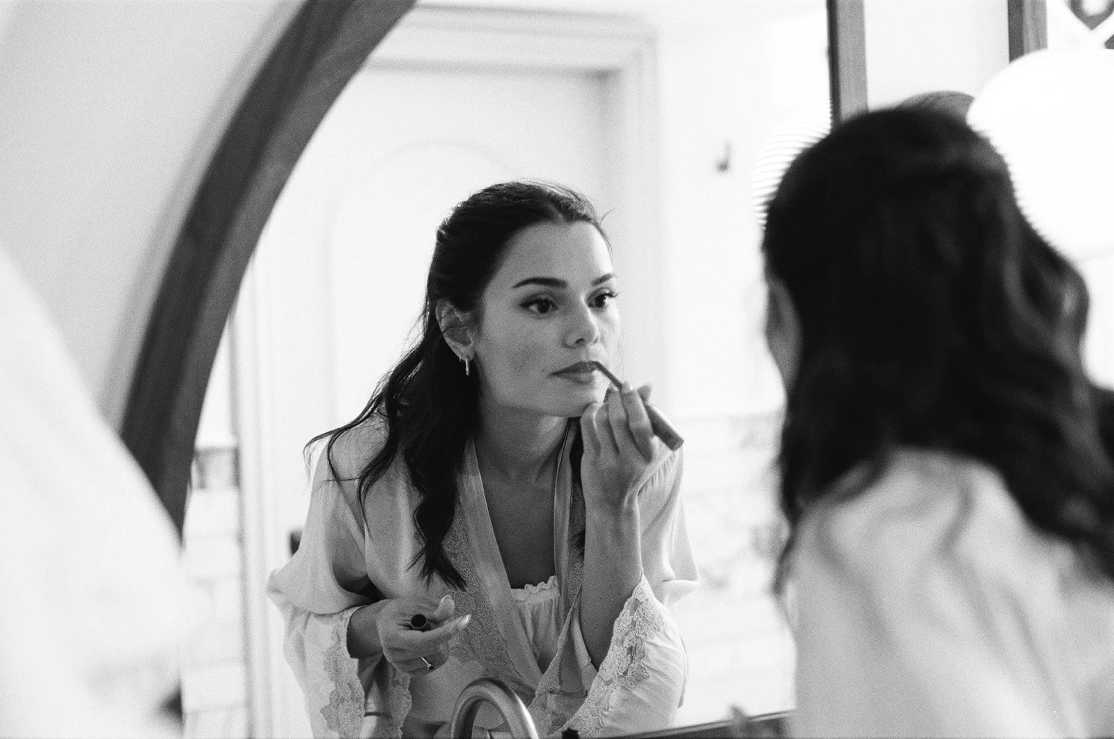 A bride getting ready at the Bull in Burford for her wedding at Worton Kitchen Garden. She is looking in the mirror and doing her lipstick.