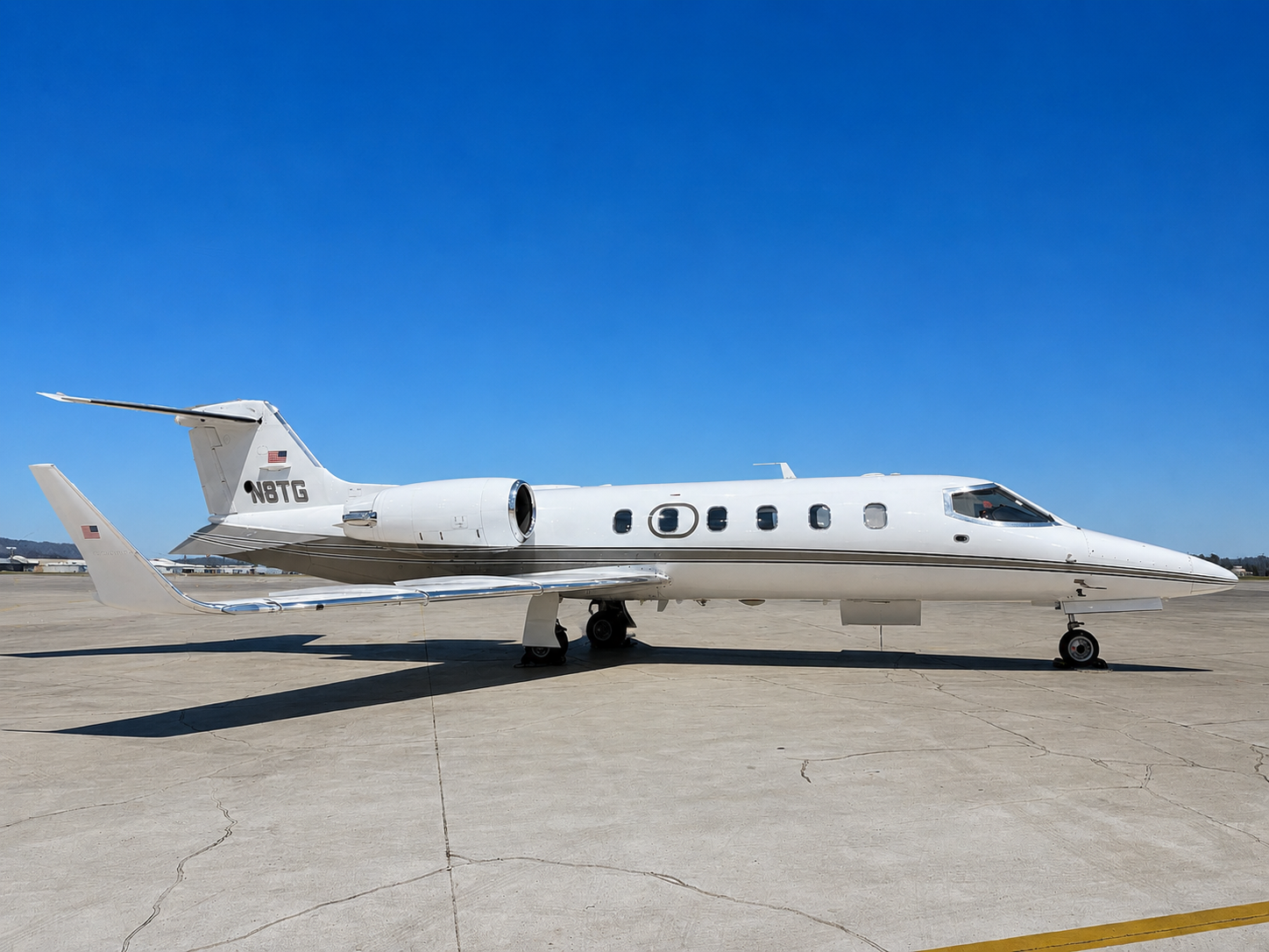 A white private jet airplane parked on the tarmac under a clear blue sky.