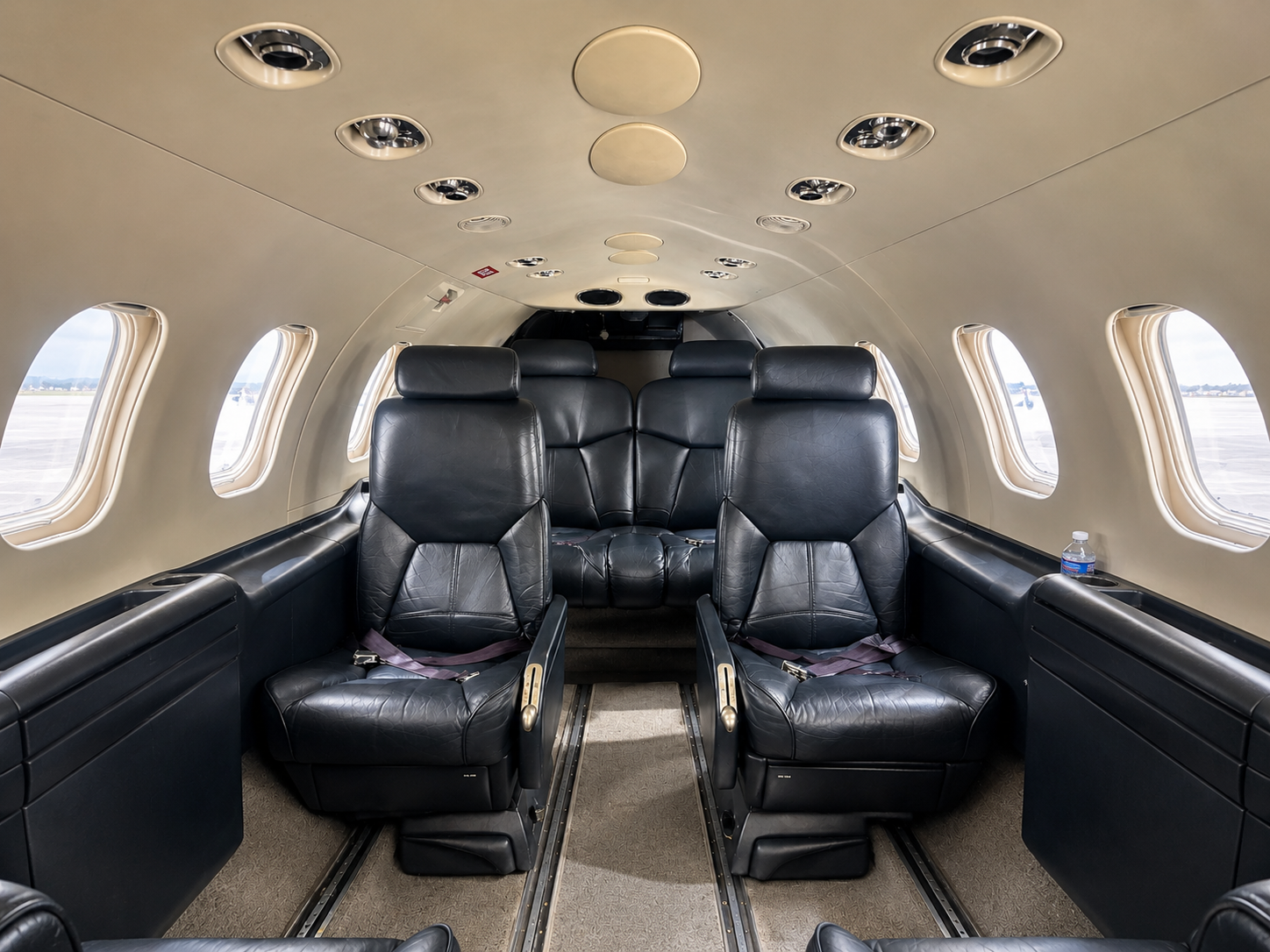 Interior of a private jet with black leather seats and small windows showing an airport runway.