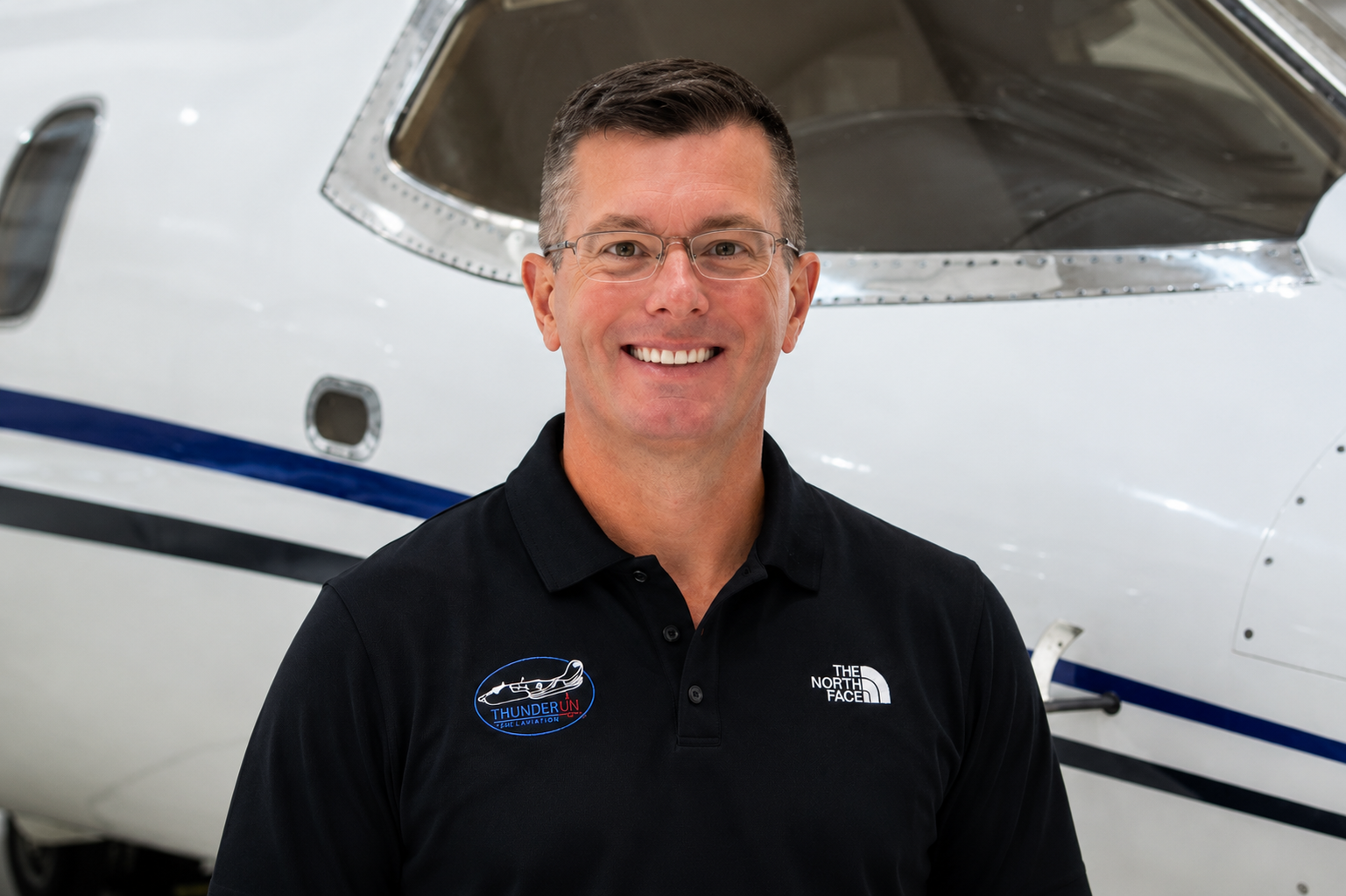 Man smiling in front of a spacecraft wearing a black polo shirt with NASA logos.