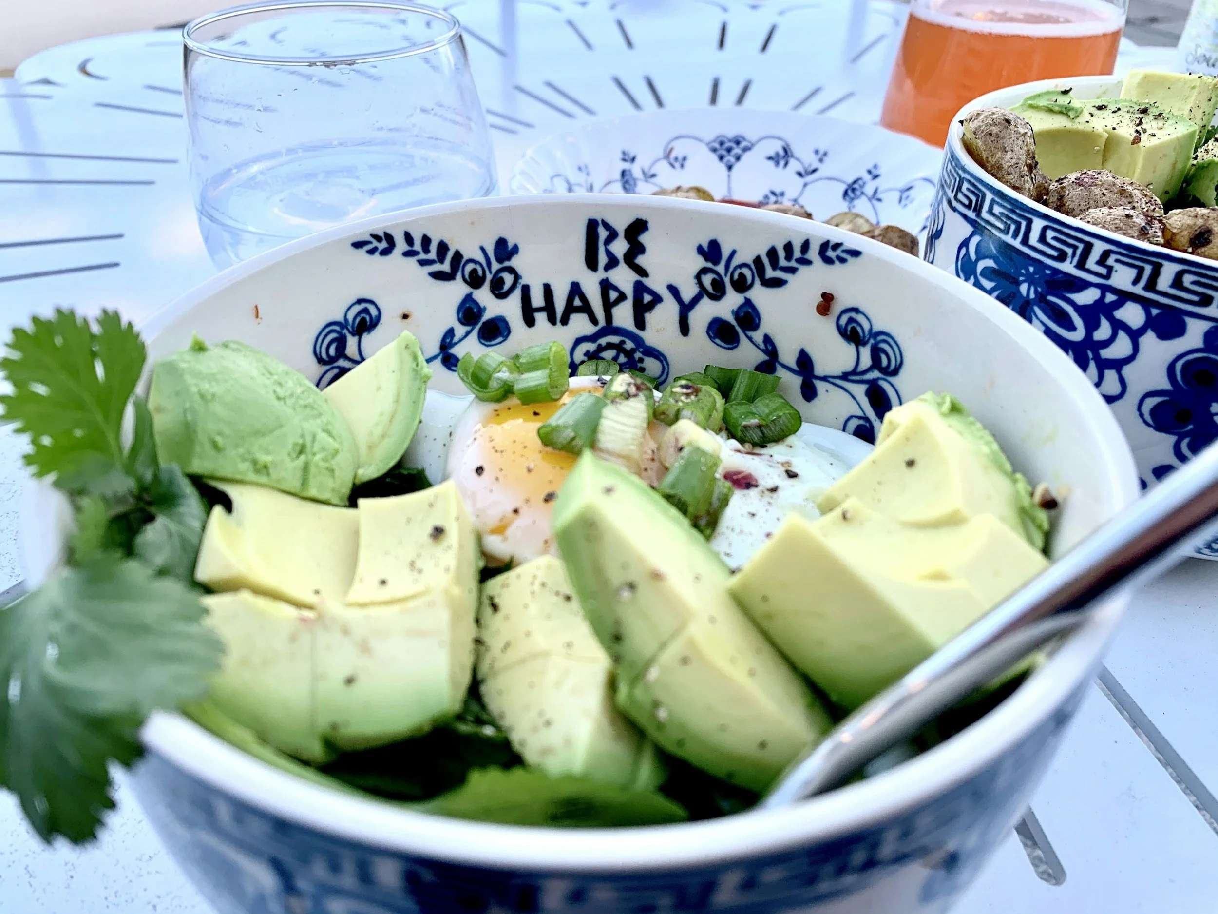 avocado and an egg in a white bowl with Be Happy written in blue.