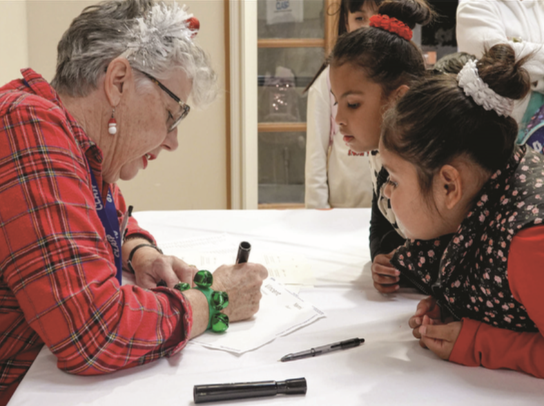 Woman writing while two children look on.