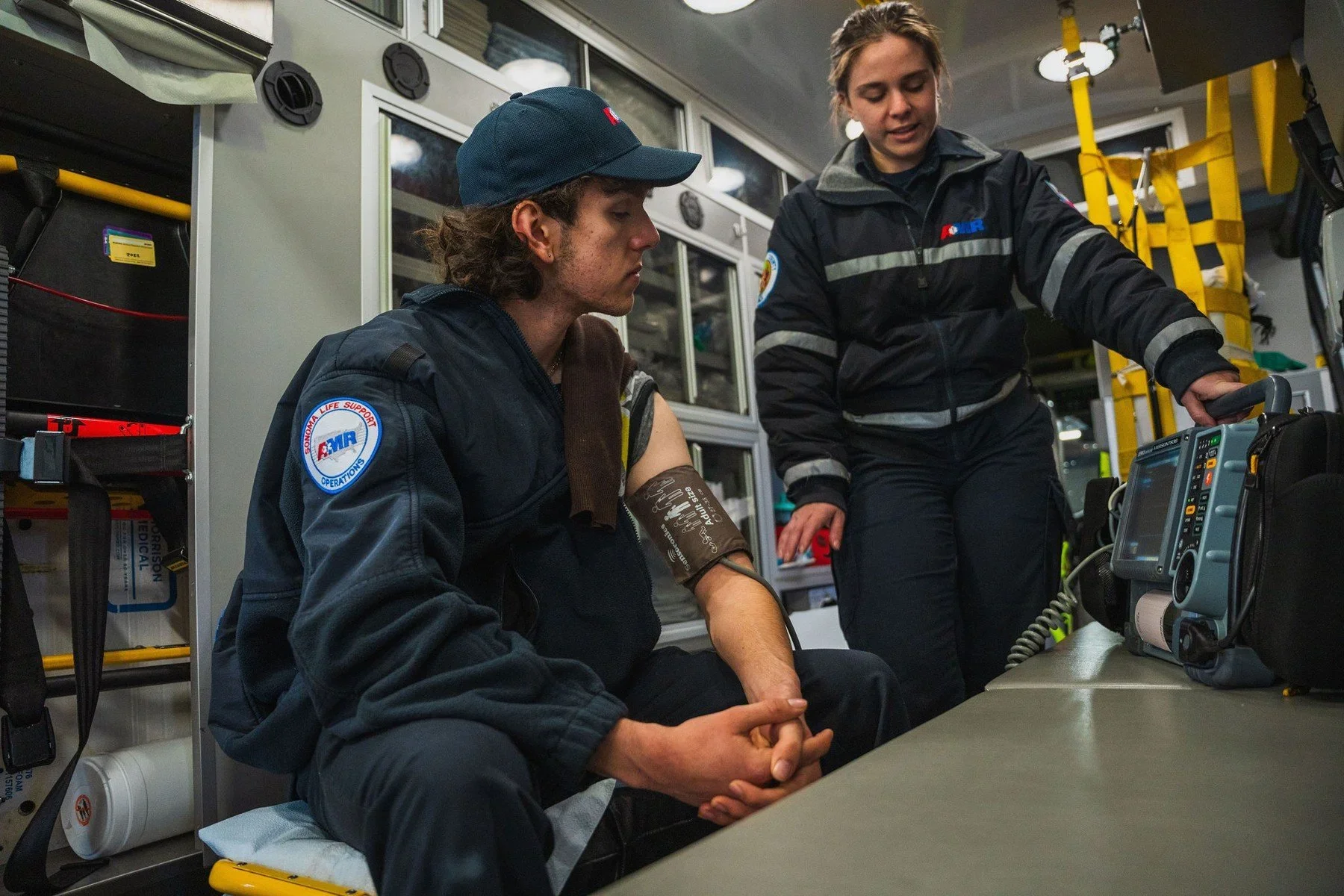 A mentor demonstrating a blood pressure monitor inside an ambulance