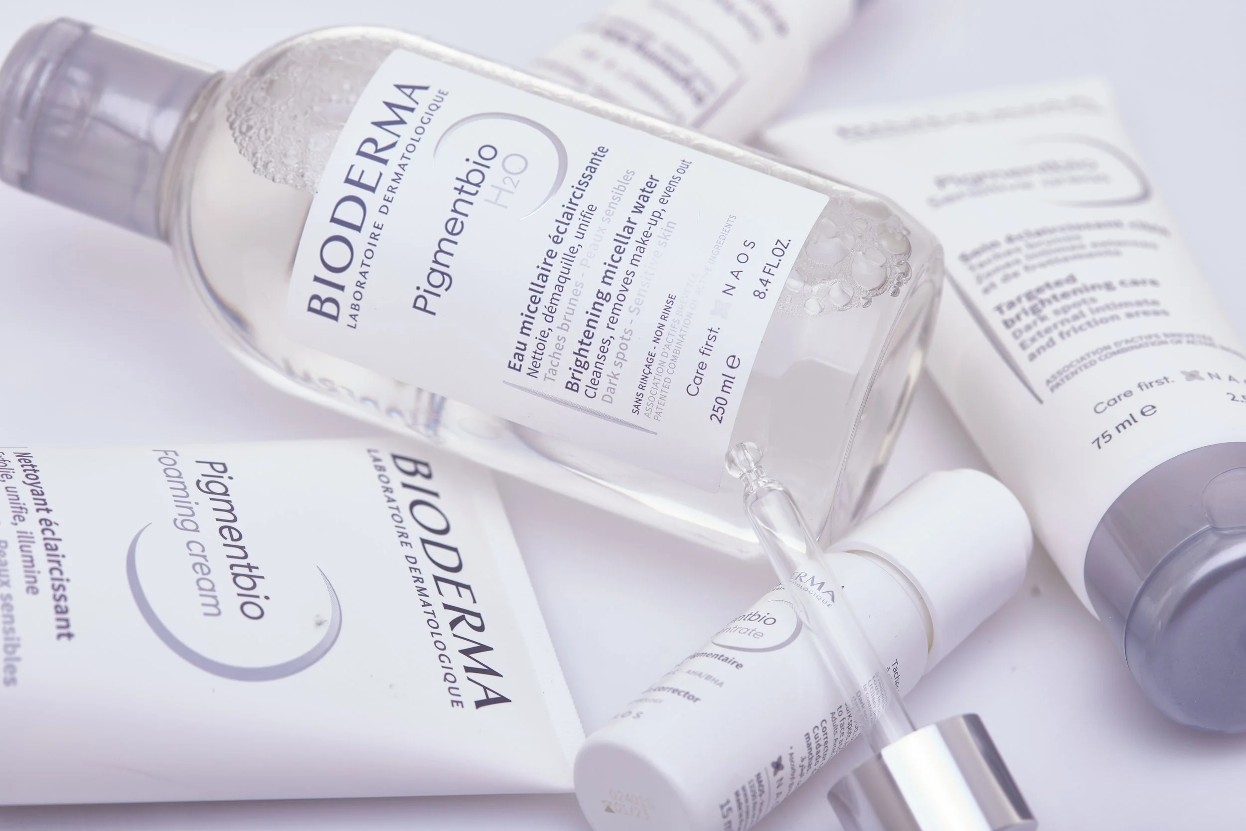 Diversos produtos de cuidados com a pele da marca Bioderma, incluindo um frasco de água micelar e outros itens de embalagem branca com texto em francês.