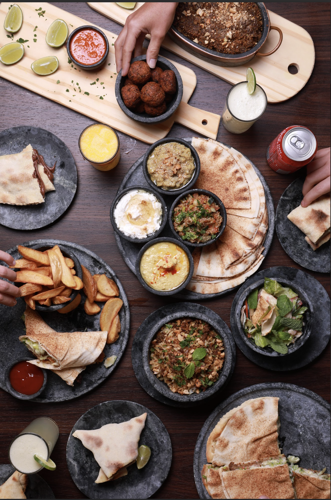 Mesa de comida mexicana com pratos como guacamole, salsa, frijoles, burritos, tacos, nachos, batatas fritas e outras tortilhas, acompanhada de limonadas e refrigerantes.