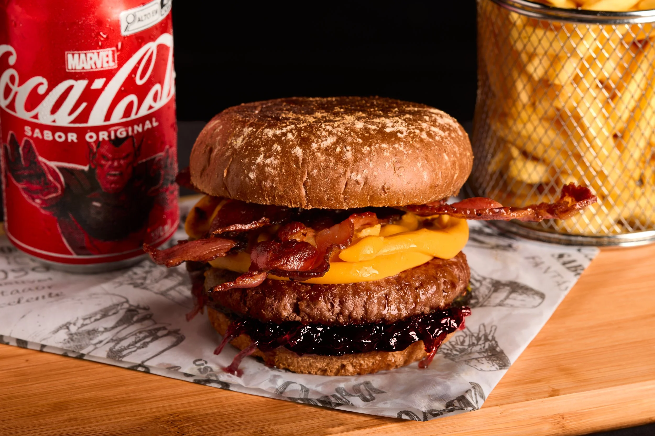 Hambúrguer com queijo, bacon, molho, hambúrguer de carne e pão, acompanhado de batatas fritas e uma lata de Coca-Cola