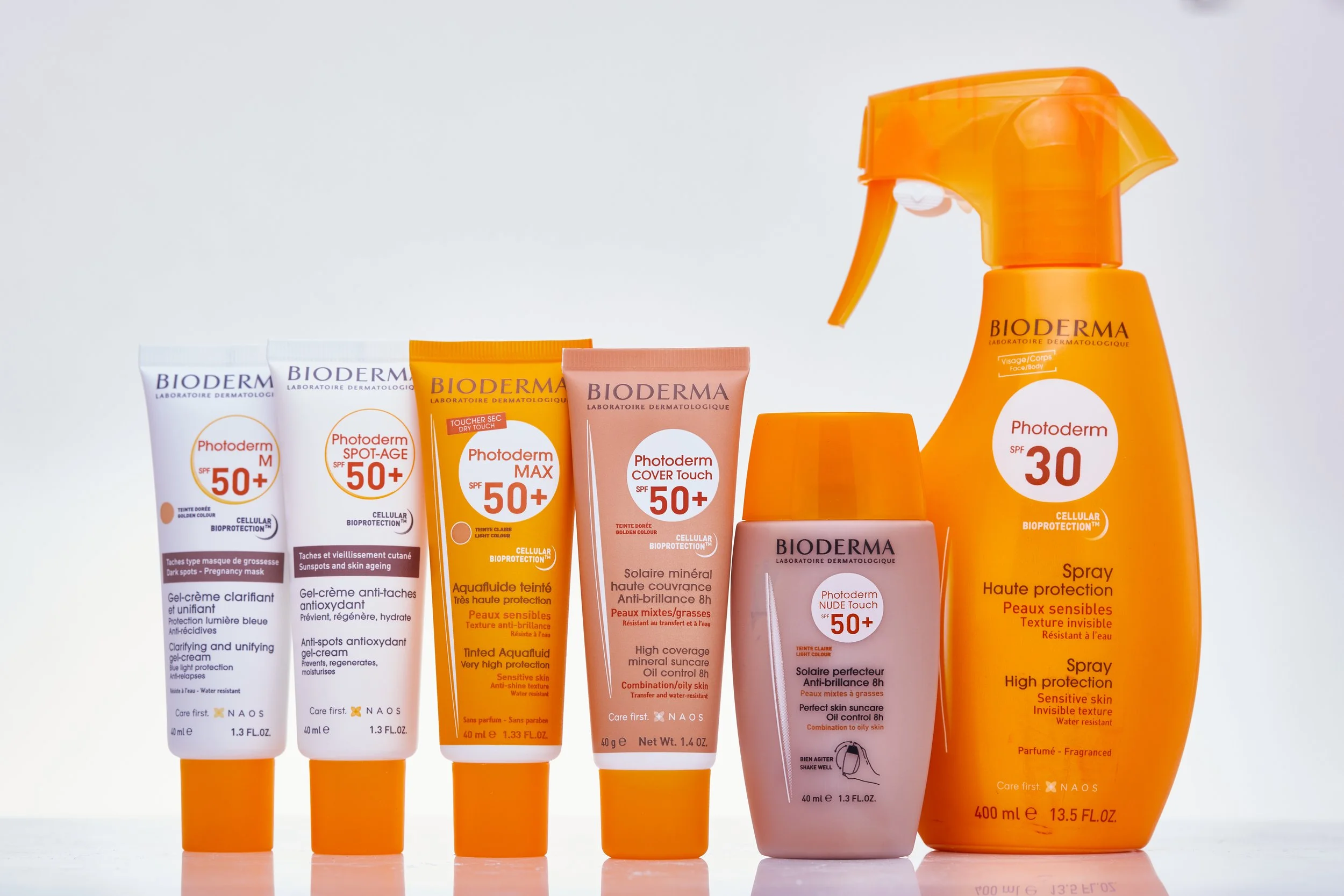 Diversos produtos de proteção solar da Bioderma, incluindo loções, sprays e cremes com SPF 50+ e SPF 30, dispostos sobre uma superfície branca.