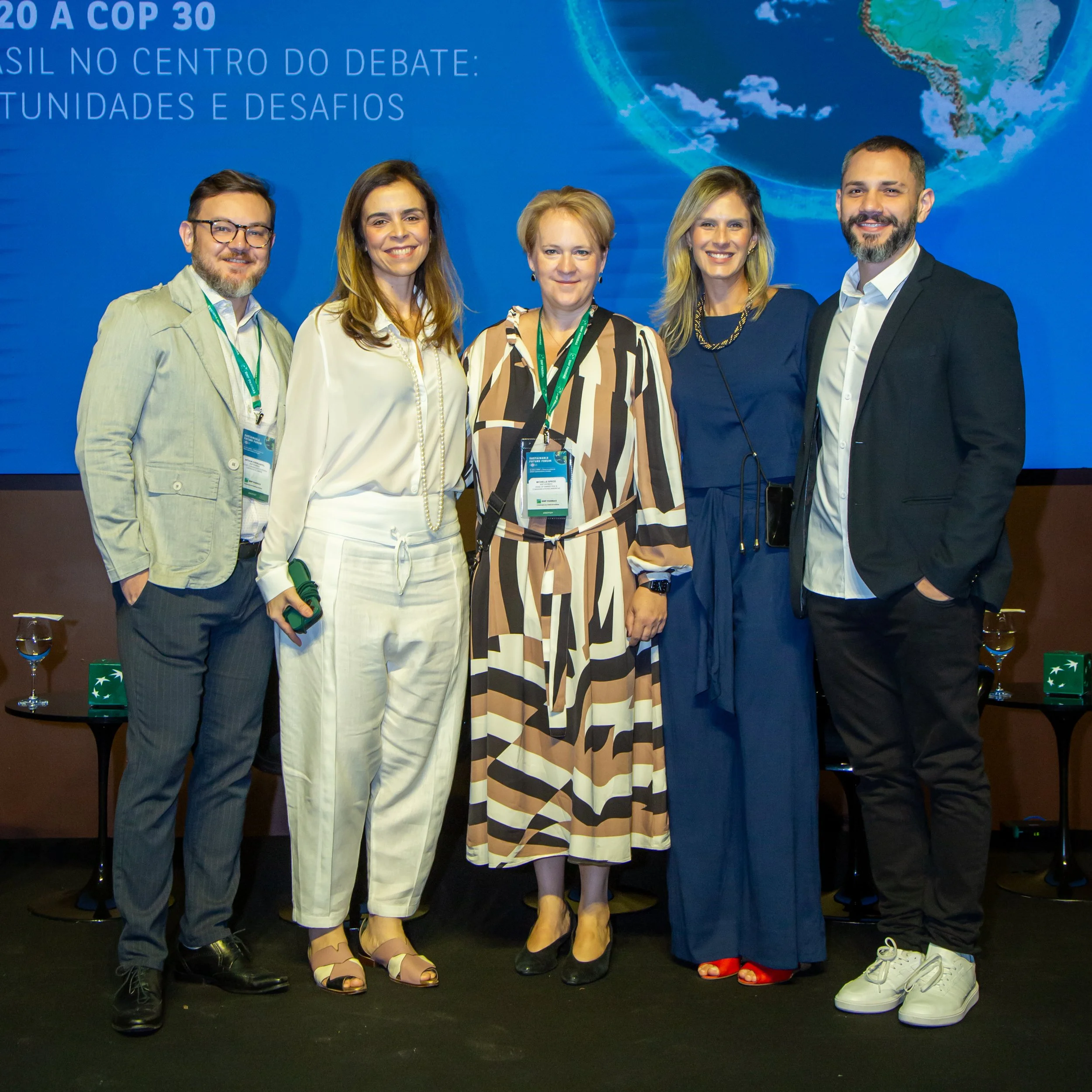 Grupo de cinco pessoas posando para fotografia em evento, com um fundo exibindo o mapa do Brasil e texto em português.