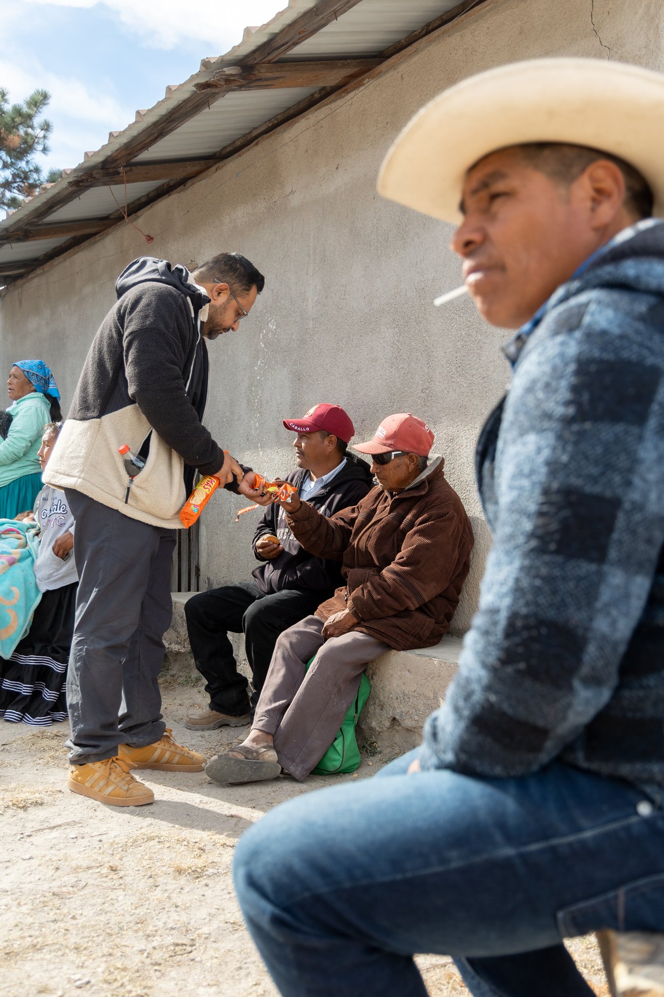 A man handing out snacks to seated older men against a wall outdoors - Sasha at REDFISH | Creative Studio
