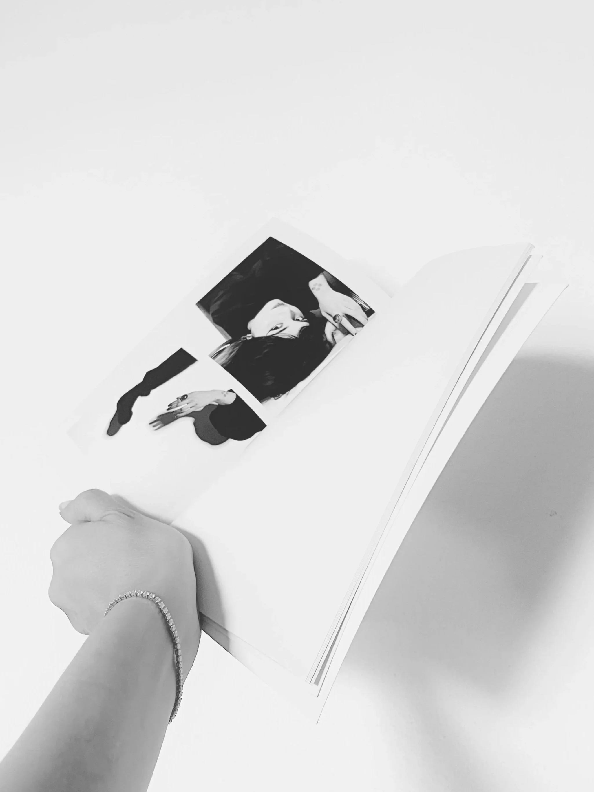 A black and white photo of a hand holding up an open copy of the book "Still Life" by Menna Awad