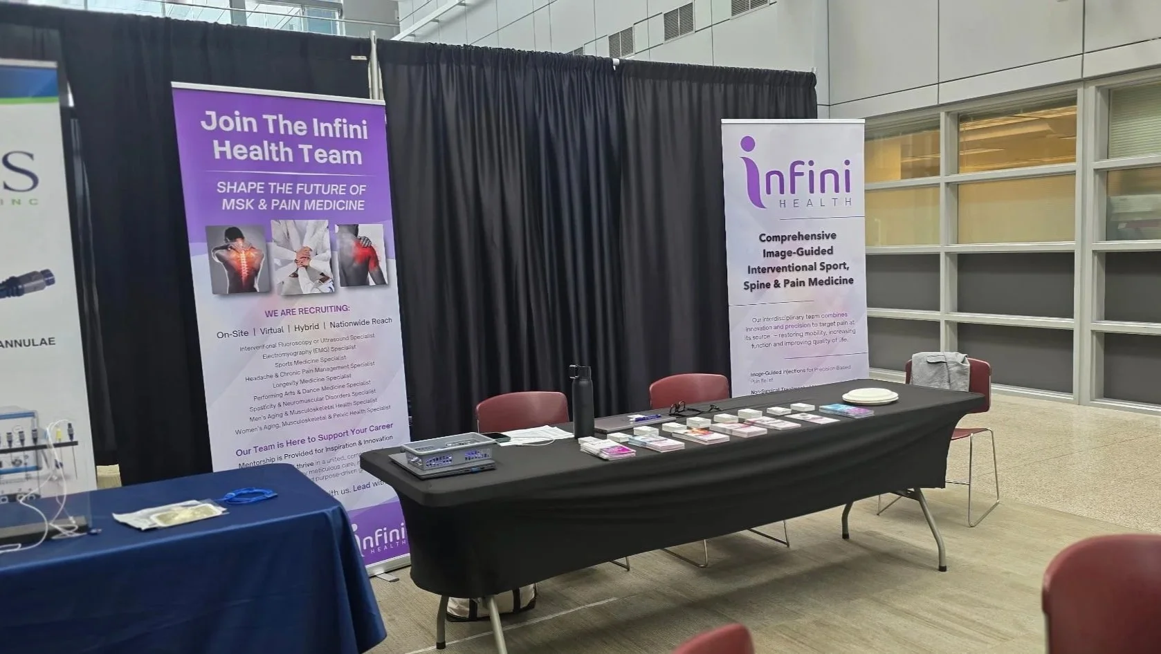 Exhibition booth for InfinI Health at a conference, with banners about health services and a table with informational materials and pamphlets.