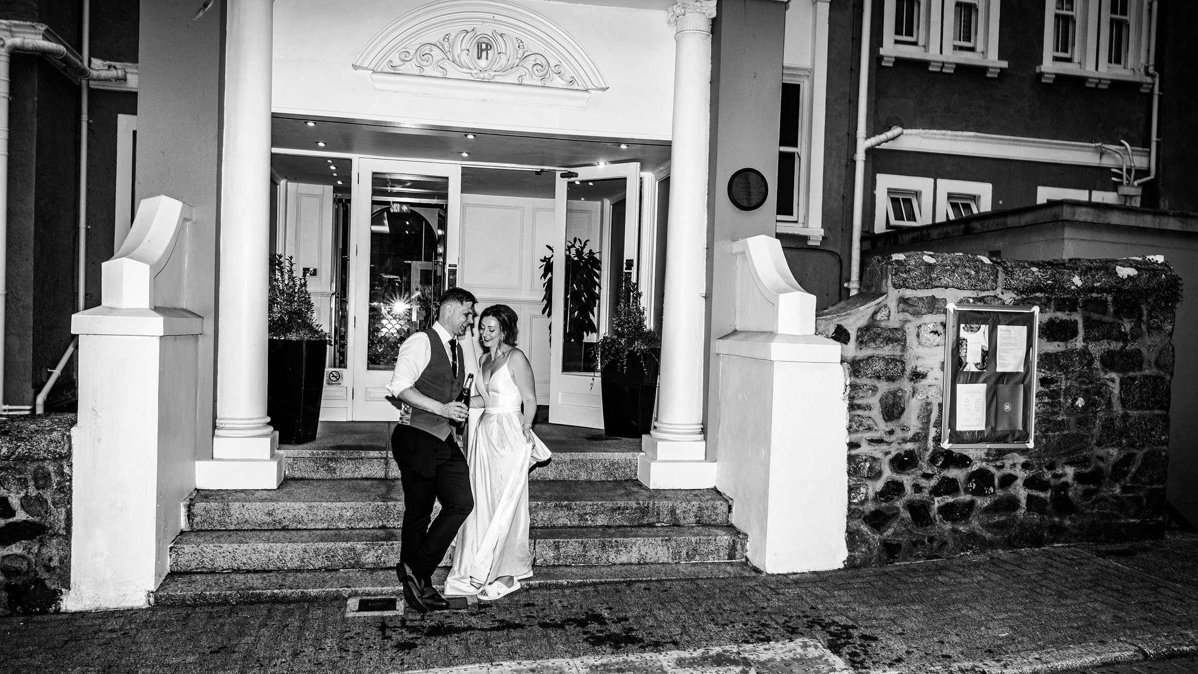 Two people, a man and a woman, standing and talking on the steps outside the St Ives Harbour Hotel. Wedding photo by Oliver Harris Photography.