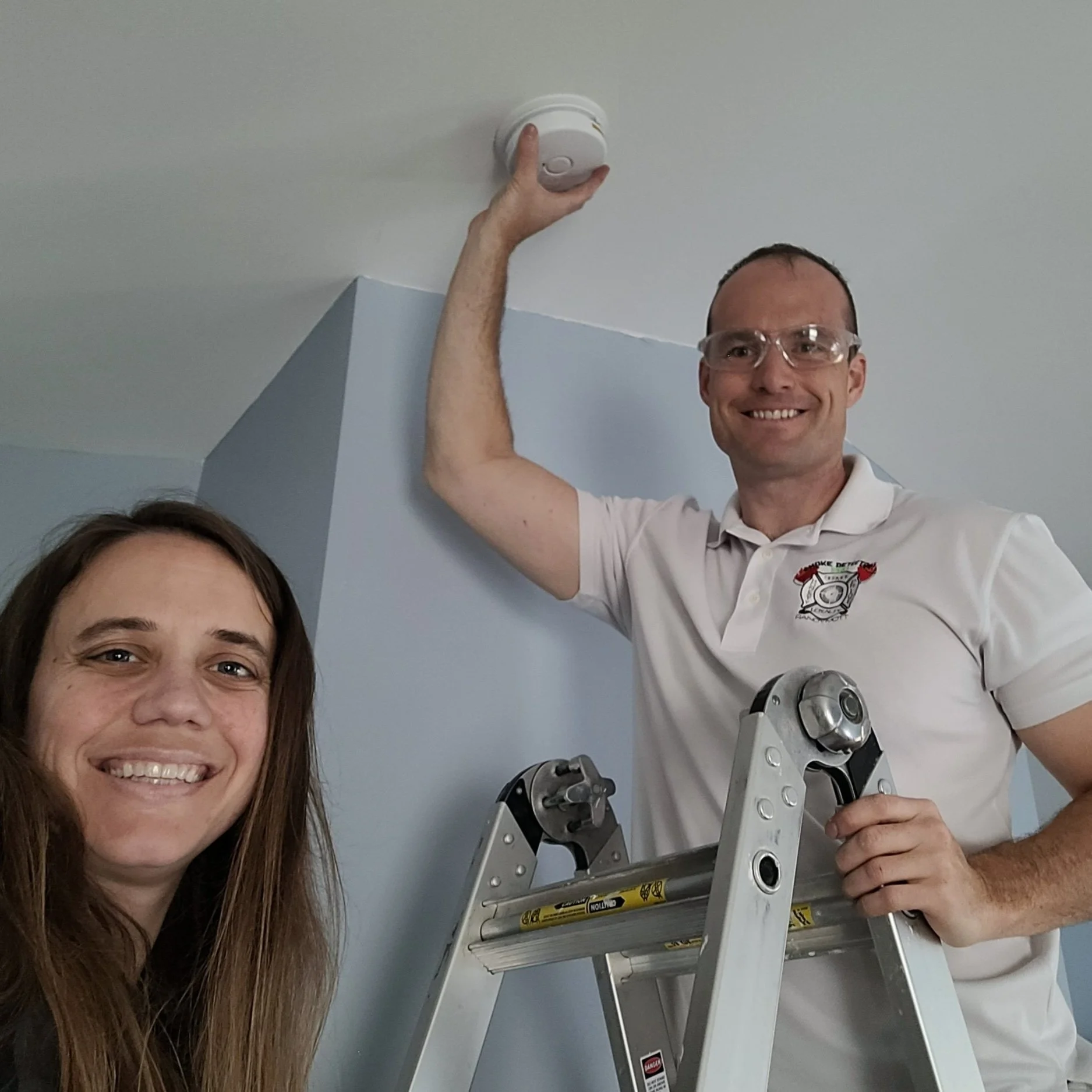 a happy customer smiling in a picture as Smoke Detector Pro technician replaces a smoke alarm in Lake Saint Louis MO