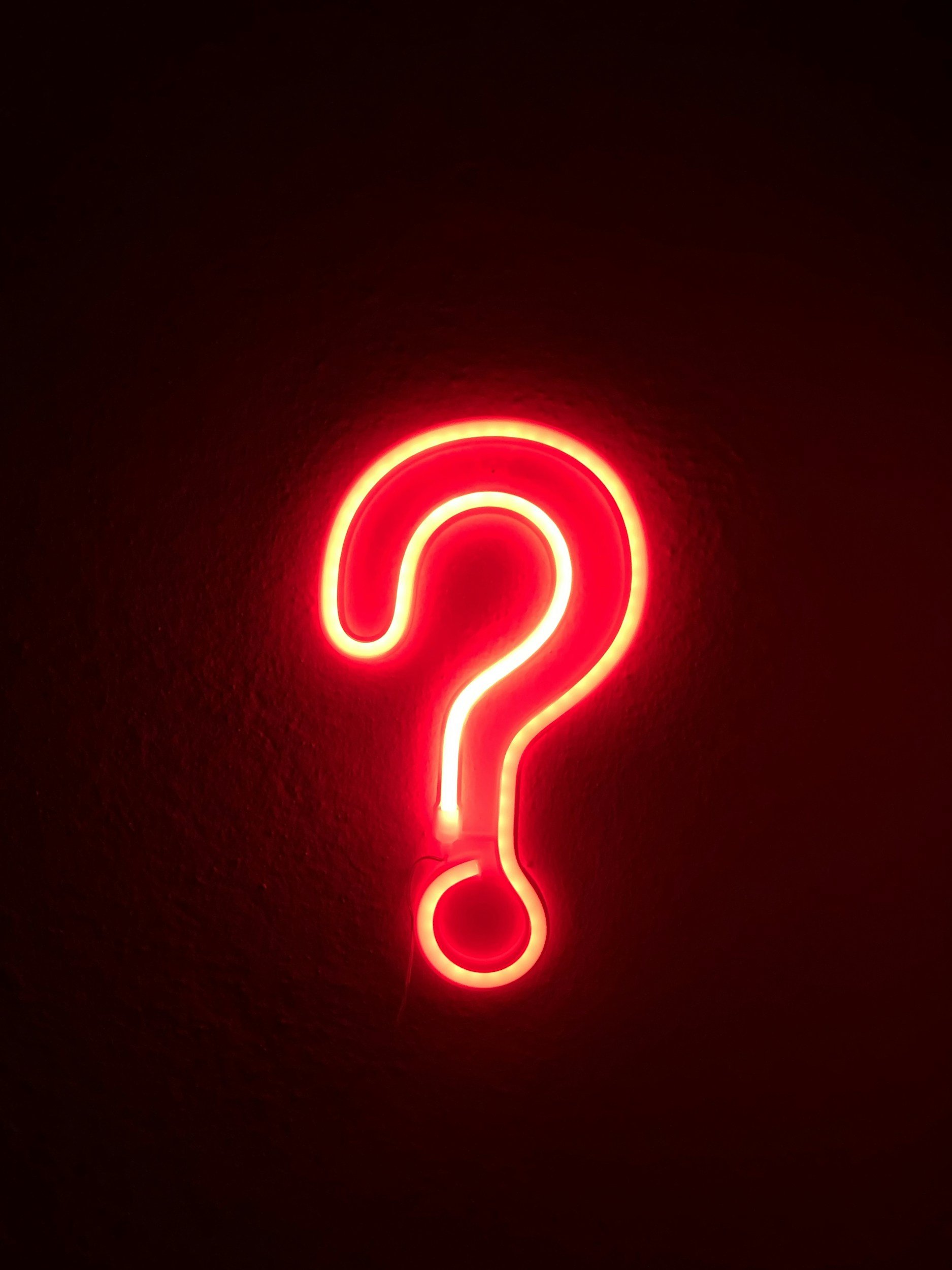 Red neon light in the shape of a question mark on a black background.
