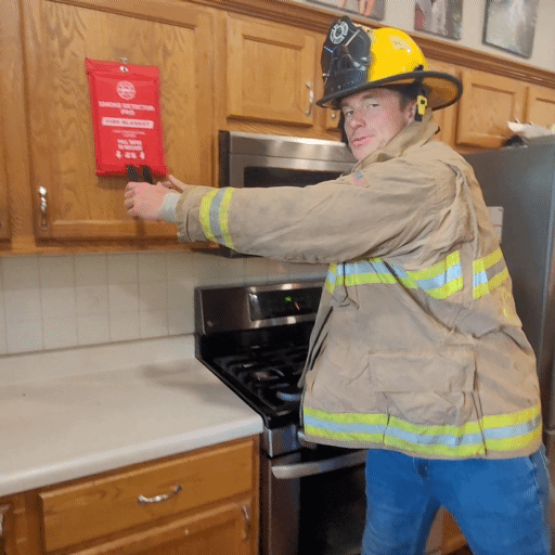 Firefighter in kitchen using a fire blanket to put out a fire.