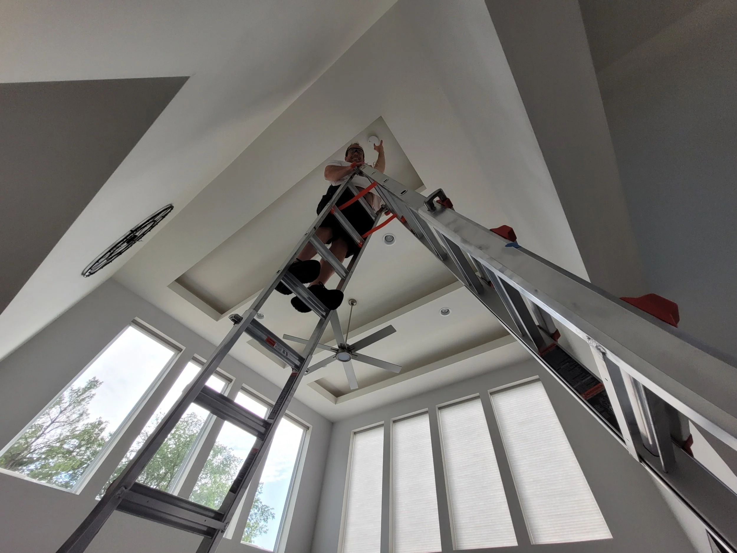 picture of Smoke detector pro on a ladder in a home in Saint Charles County MO with a very high ceiling smoke detector replacement