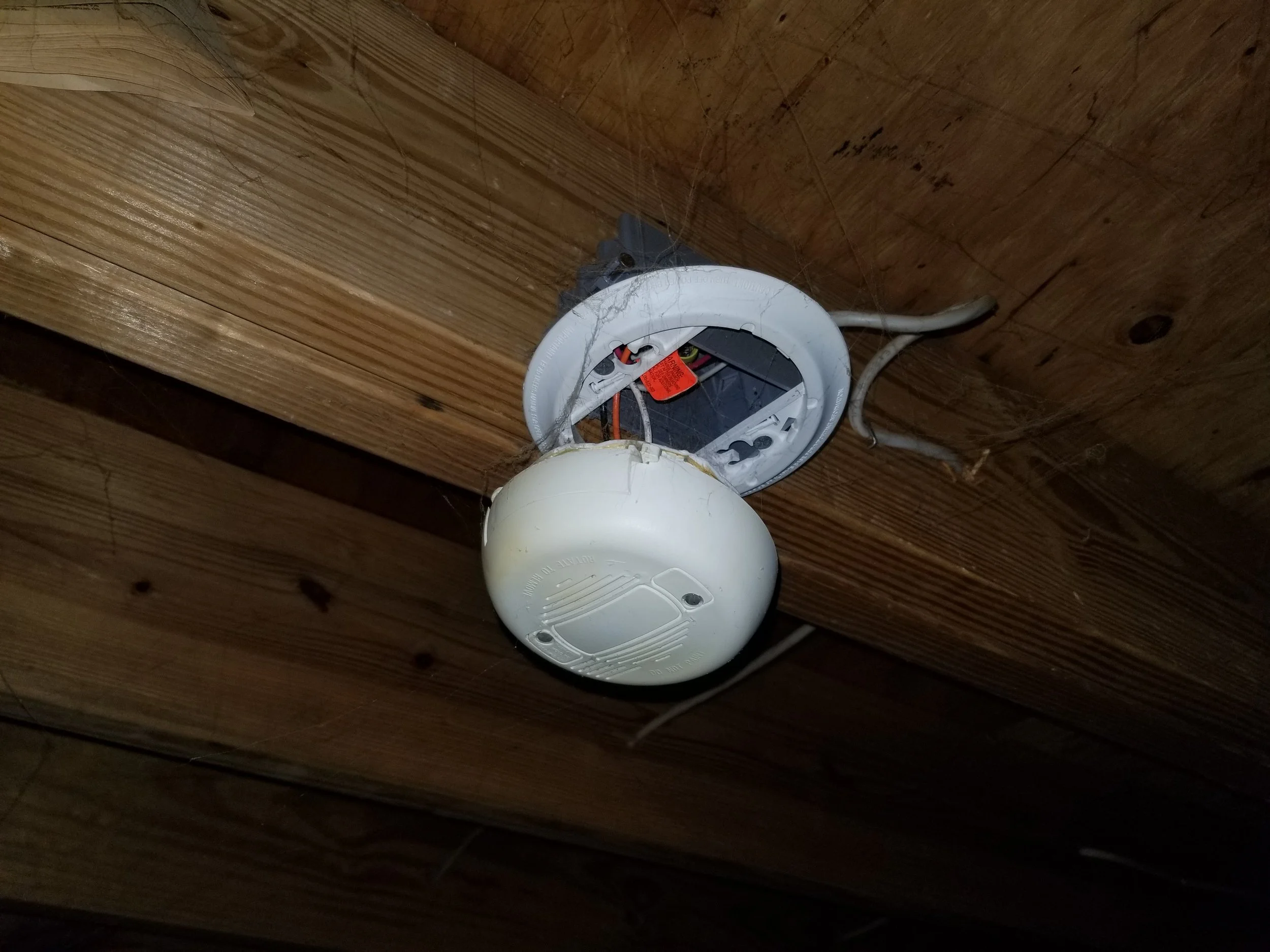 Disassembled smoke detector and electrical wiring on a wooden ceiling.