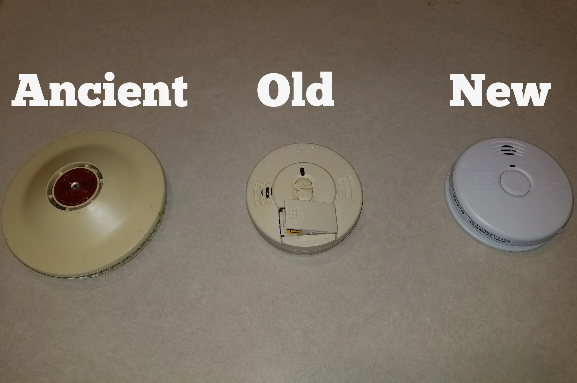 Three types of smoke detectors labeled "Ancient," "Old," and "New" shown side by side on a flat surface.