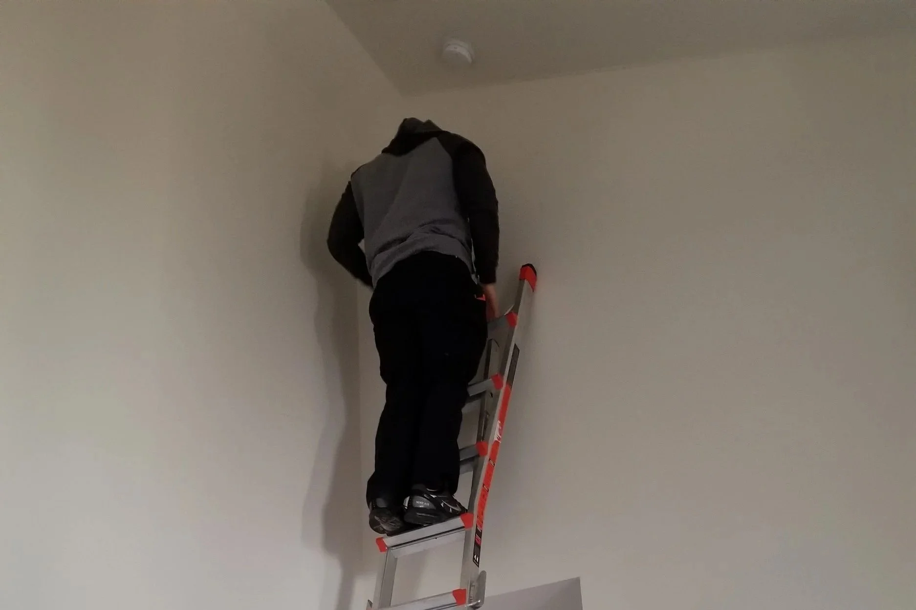 A person standing on a ladder painting a ceiling in a white room.