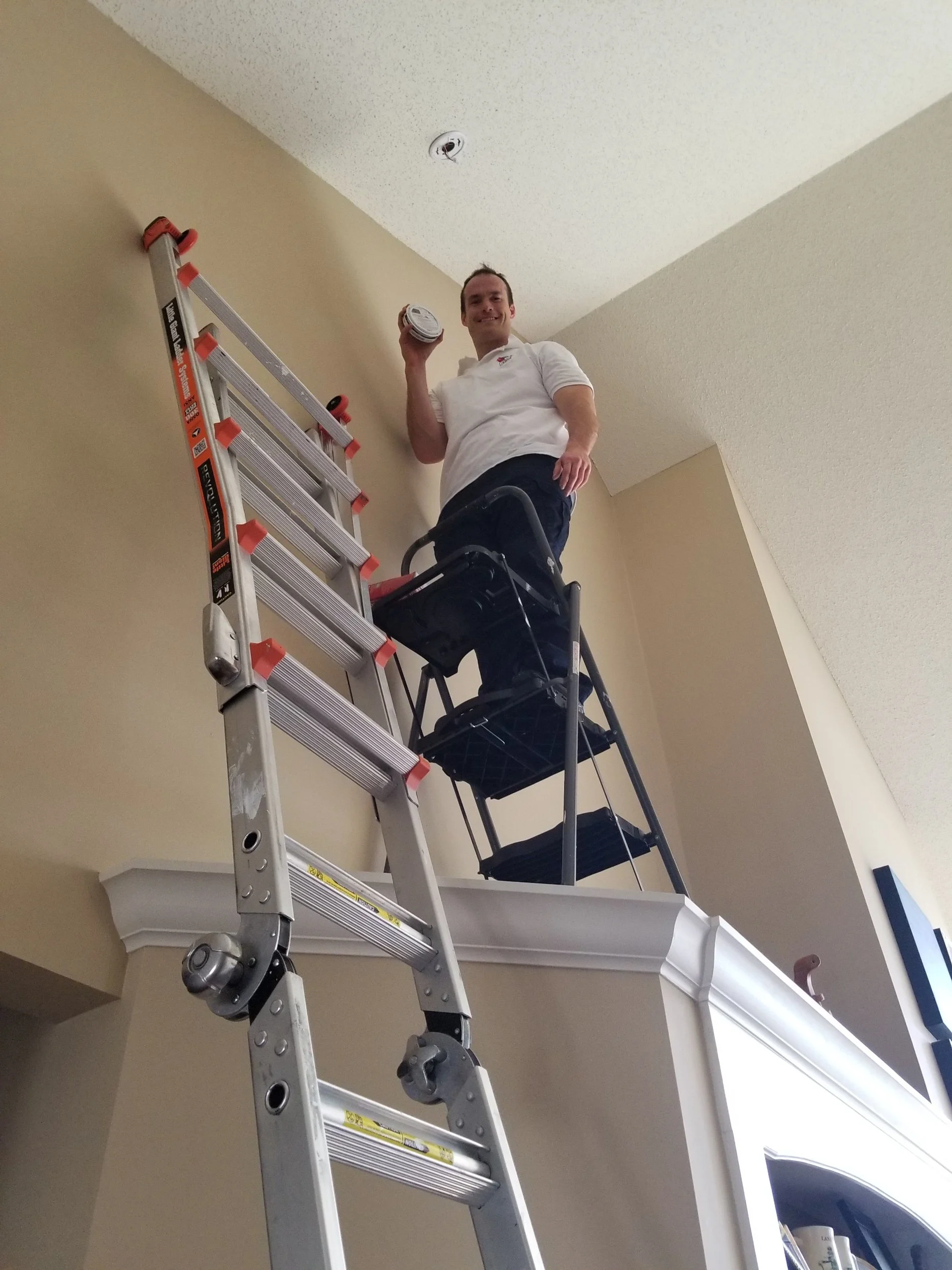 Service tech with Smoke Detector Pro, taking down a tall ceiling smoke alarm and replacing it with a new smoke alarm.