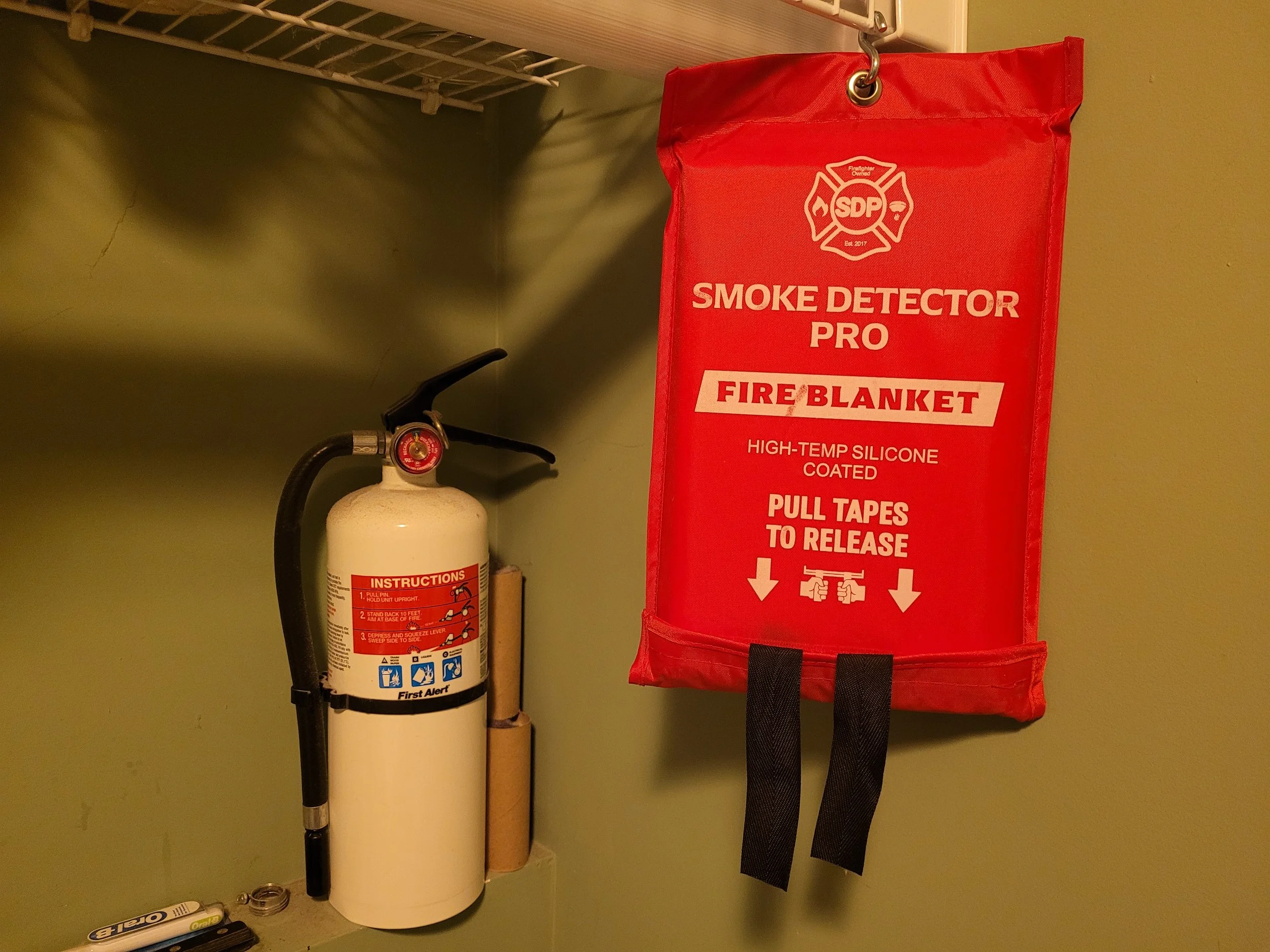 Fire extinguisher and a red fire blanket bag hanging on a wall.
