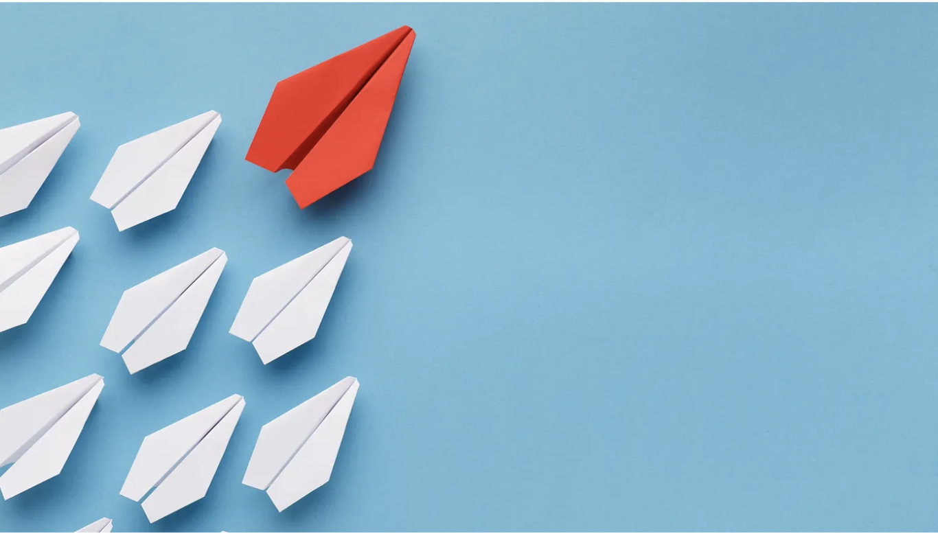 A red paper plane leading a group of white paper planes against a blue background