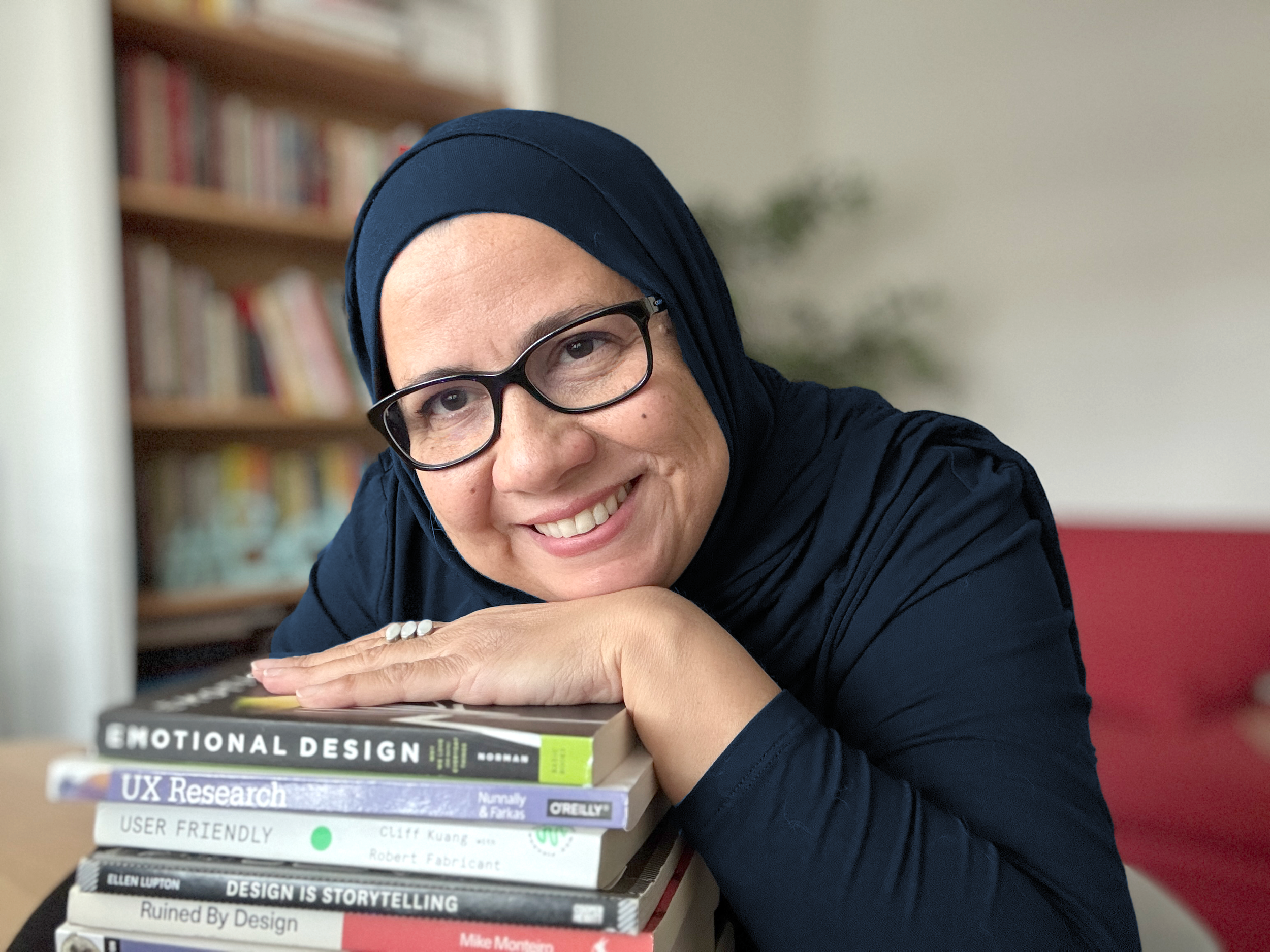Ayat Elamrawy smiling, resting her head on a stack of design and research books.